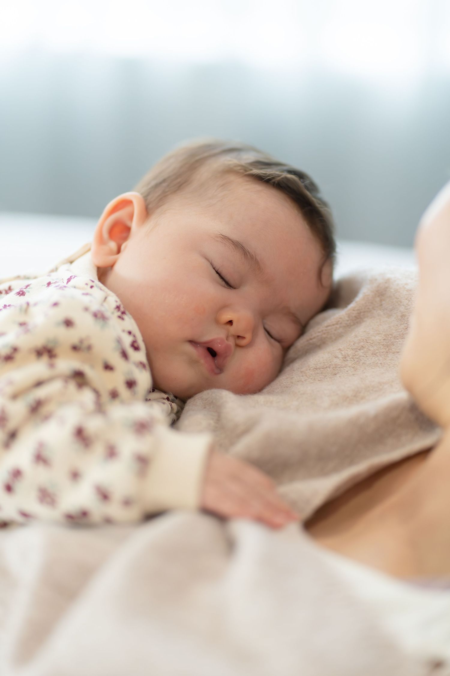Peaceful newborn baby sleeping soundly on a soft beige blanket, wearing a floral onesie.
