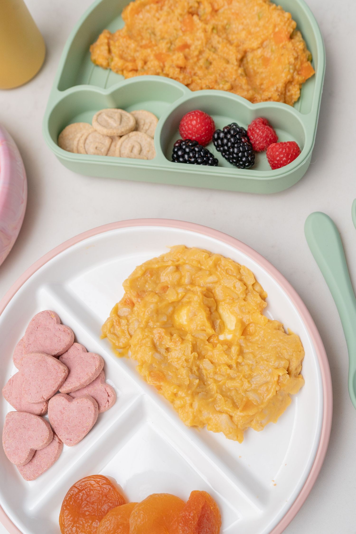 Baby meal prep plates with scrambled eggs, berries, dried apricots, and heart-shaped snacks on divided toddler plates.