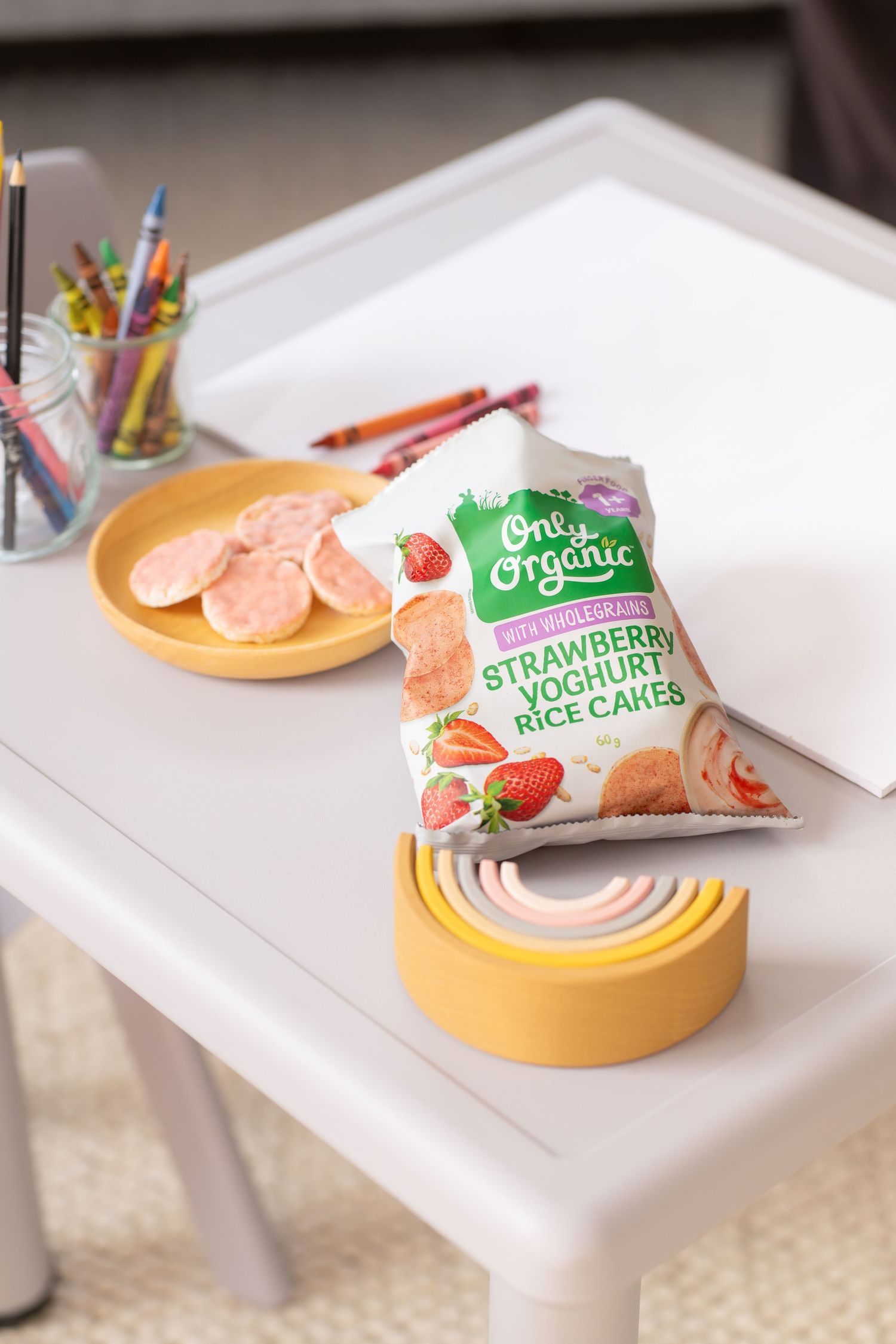 Only Organic Strawberry Yoghurt Rice Cakes bag on a white kids table with crayons and a yellow plate.