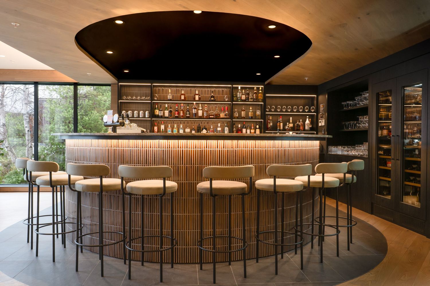 Elegant curved bar with wood paneling, backlit bottles, and cream bar stools.