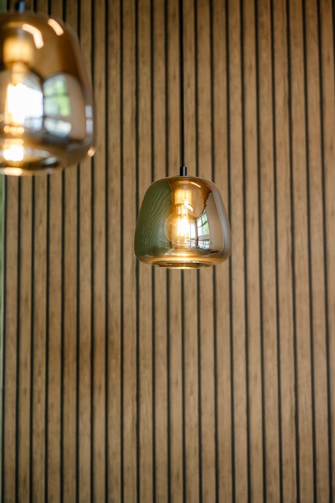 Elegant amber glass pendant light with Edison bulb hanging against wooden slat wall in modern interior.