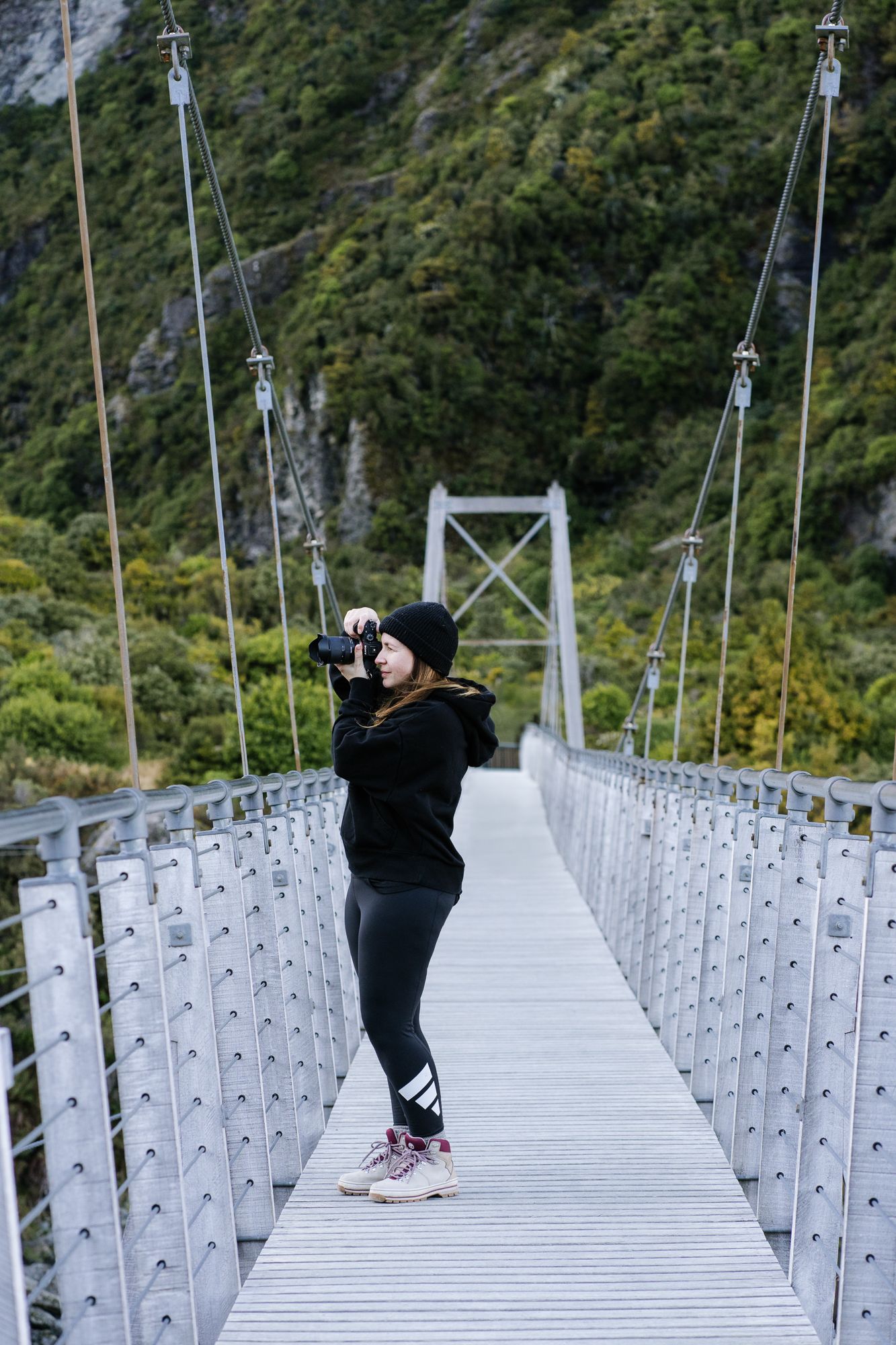 Female photographer in black outfit taking photos on a suspension bridge at Mt Cook National Park, NZ.