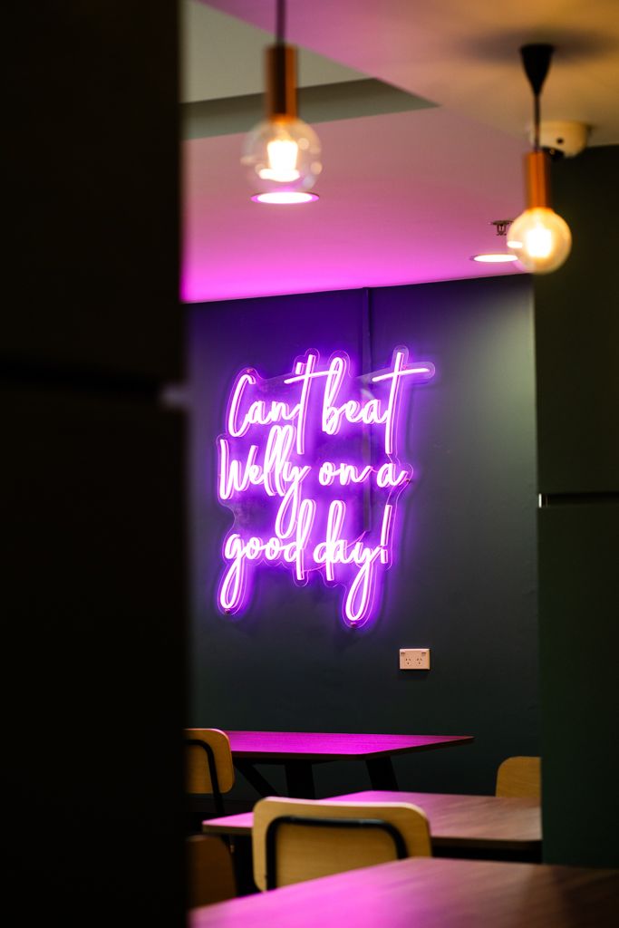 Purple neon sign reading Can't beat Welly on a good day in a dimly lit restaurant.