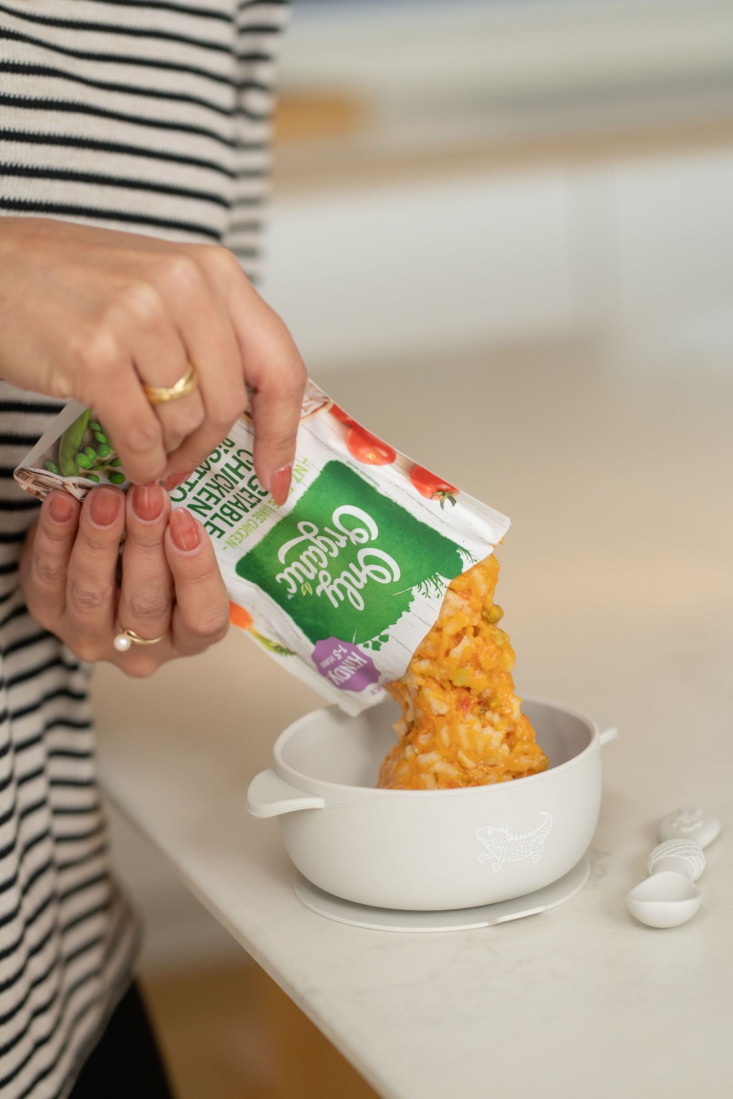 Person pouring Caly Crunchy veggie snacks from a colorful bag into a white bowl on a countertop.