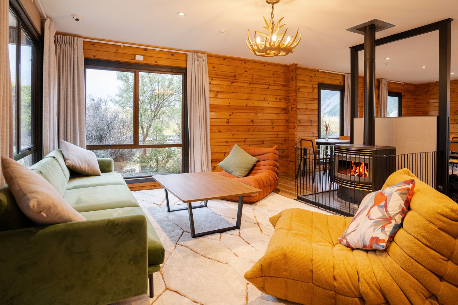 Cozy mountain chalet living room with green and yellow sofas, wood-paneled walls, and fireplace.