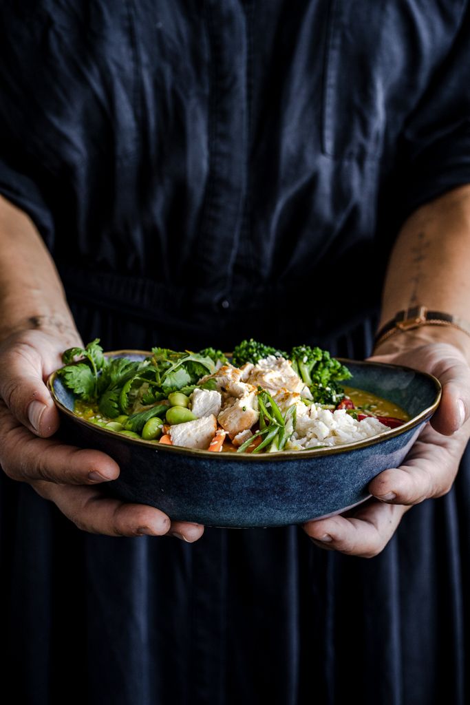 Person in dark dress holding blue ceramic bowl of fresh green salad.