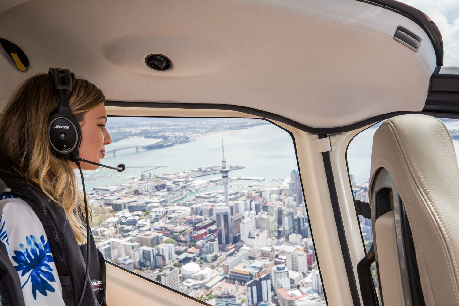 Passenger in helicopter enjoys breathtaking aerial view of Auckland city skyline and waterfront harbor.