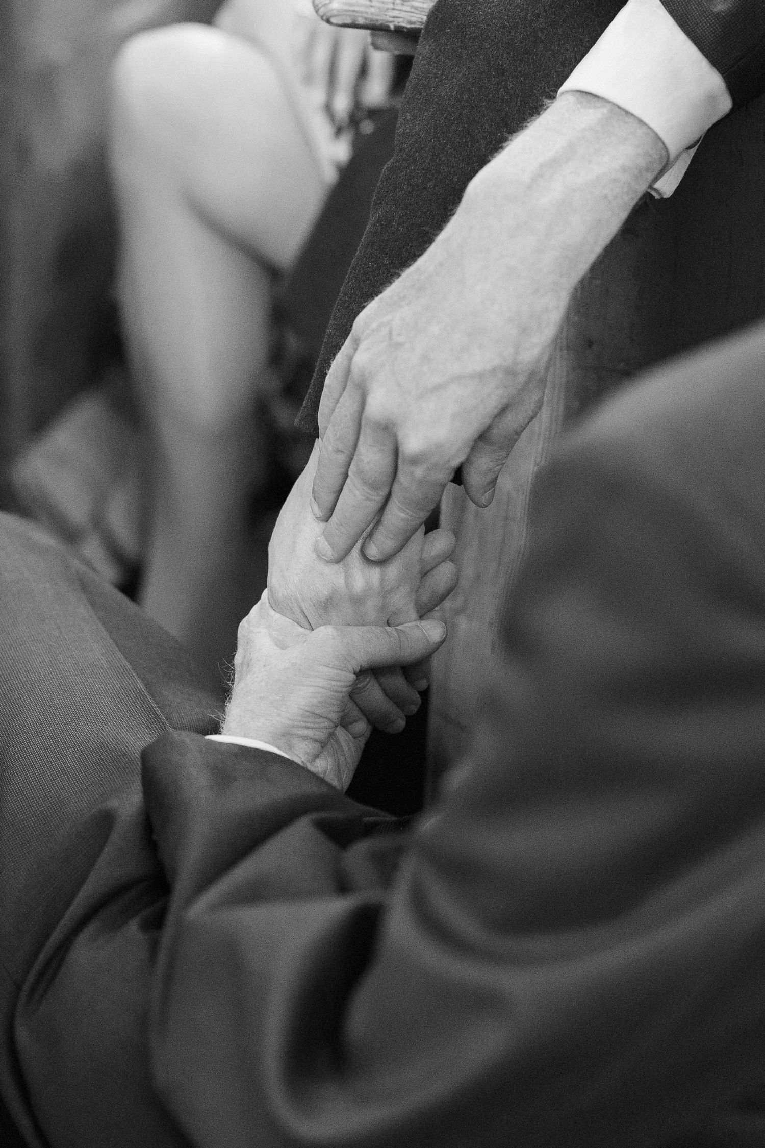 Black and white photo of two people holding hands warmly, symbolizing connection and support at a formal event.