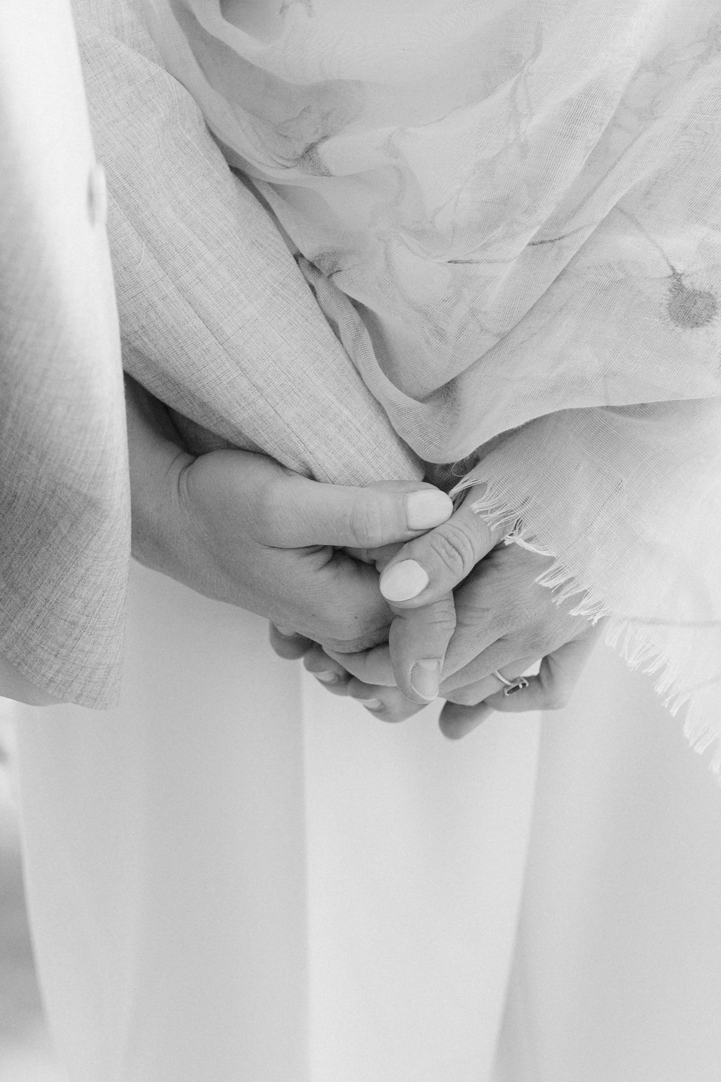 Close-up black and white photo of bride and groom holding hands at wedding ceremony.