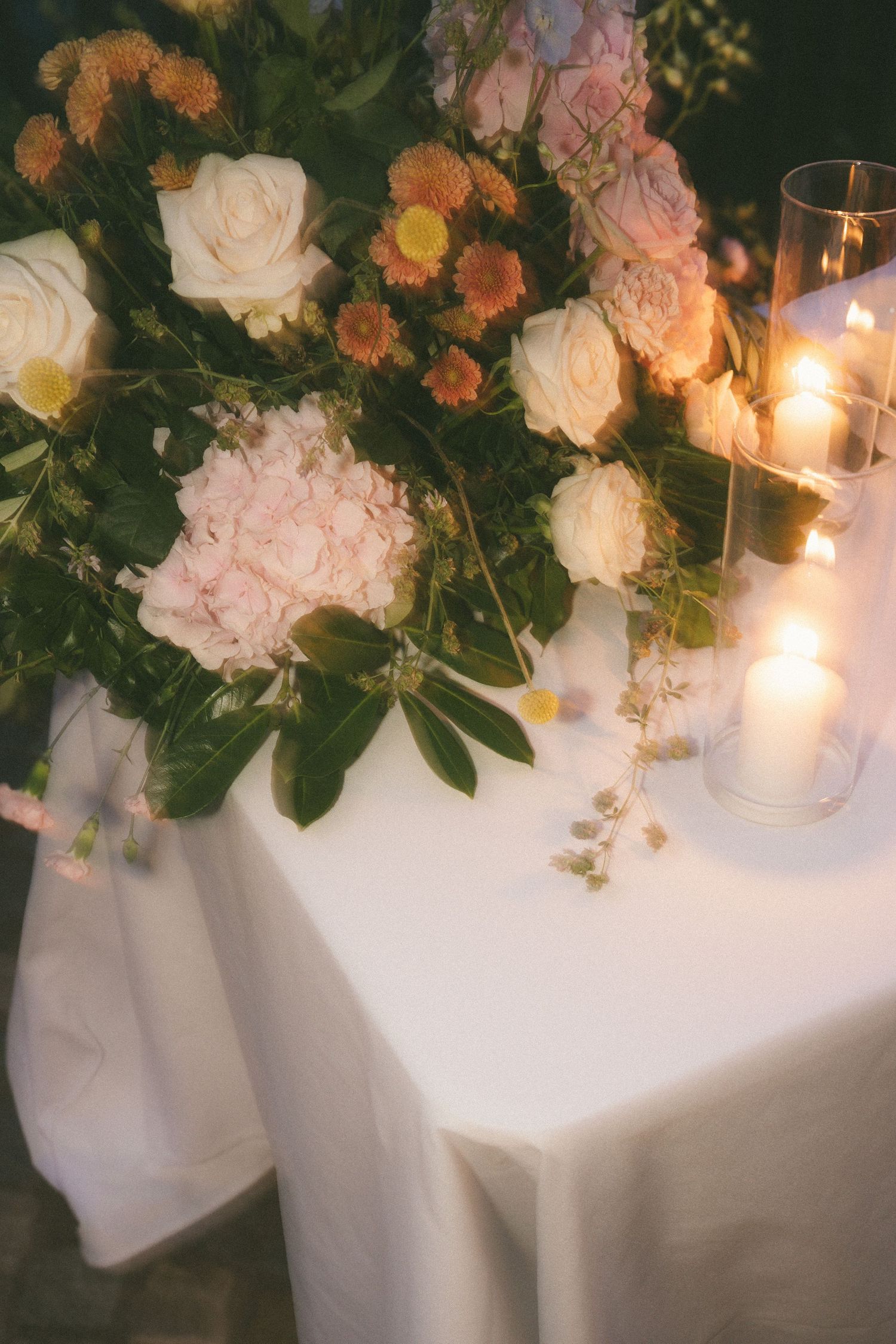 Romantic wedding table with white roses, pink hydrangeas, and glowing candles.