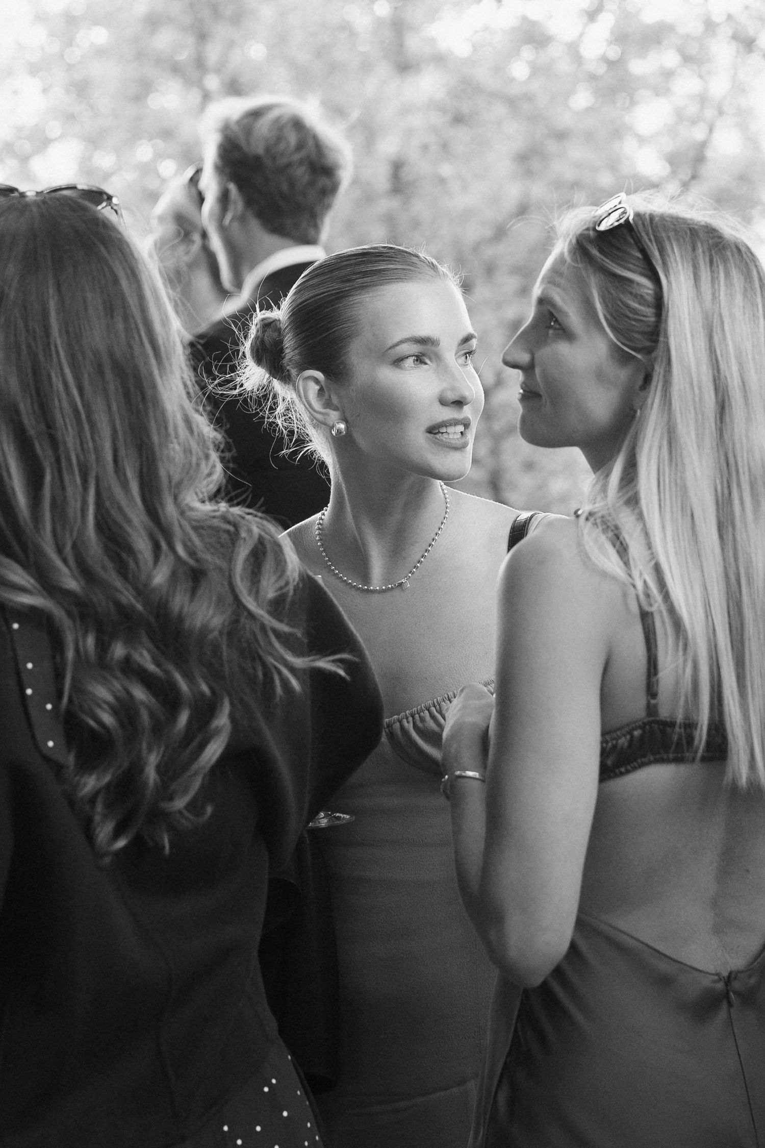 Three women in elegant dresses conversing at a wedding reception, captured in black and white.