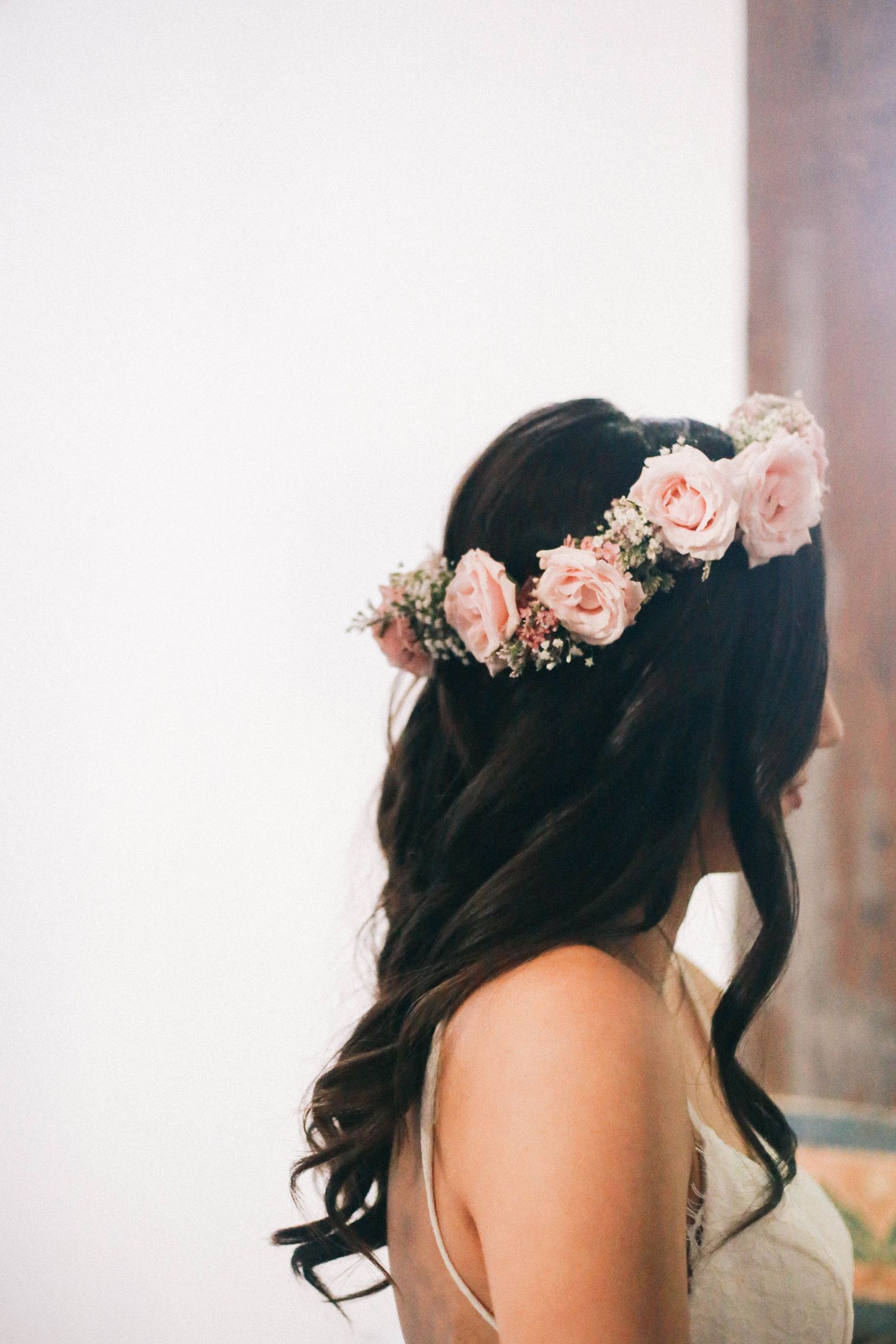 Bride with dark wavy hair adorned with a pink rose flower crown on her wedding day.