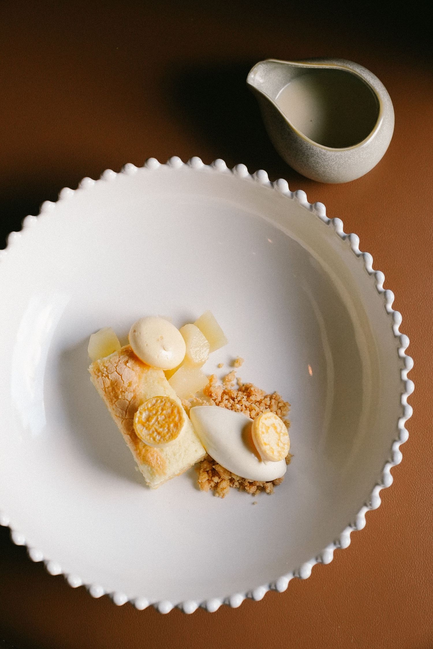 Fine dining lemon dessert with cream, crumble, and citrus slices on a white scalloped plate.