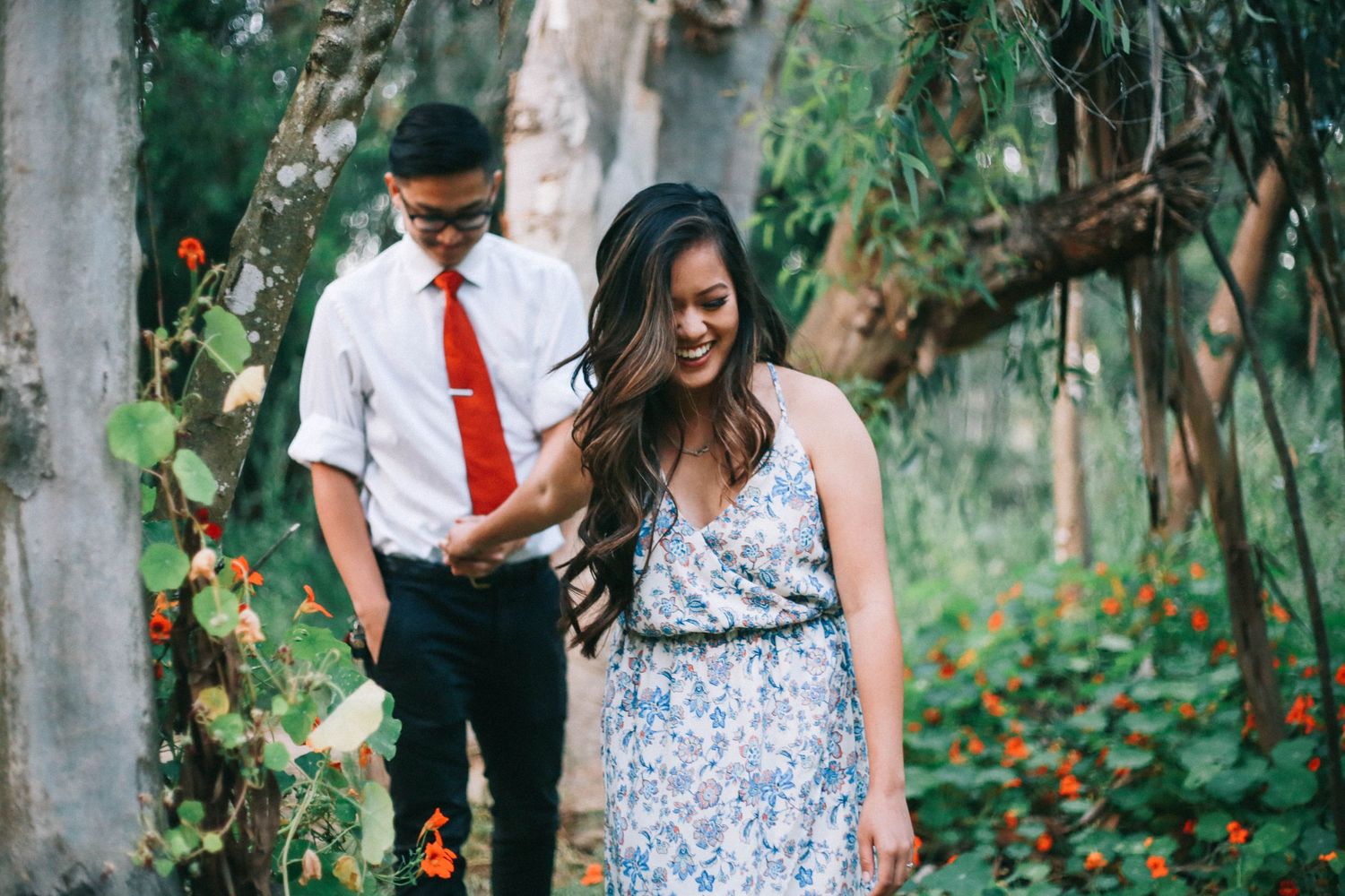 Couple walking hand in hand through a garden path surrounded by colorful flowers and trees.