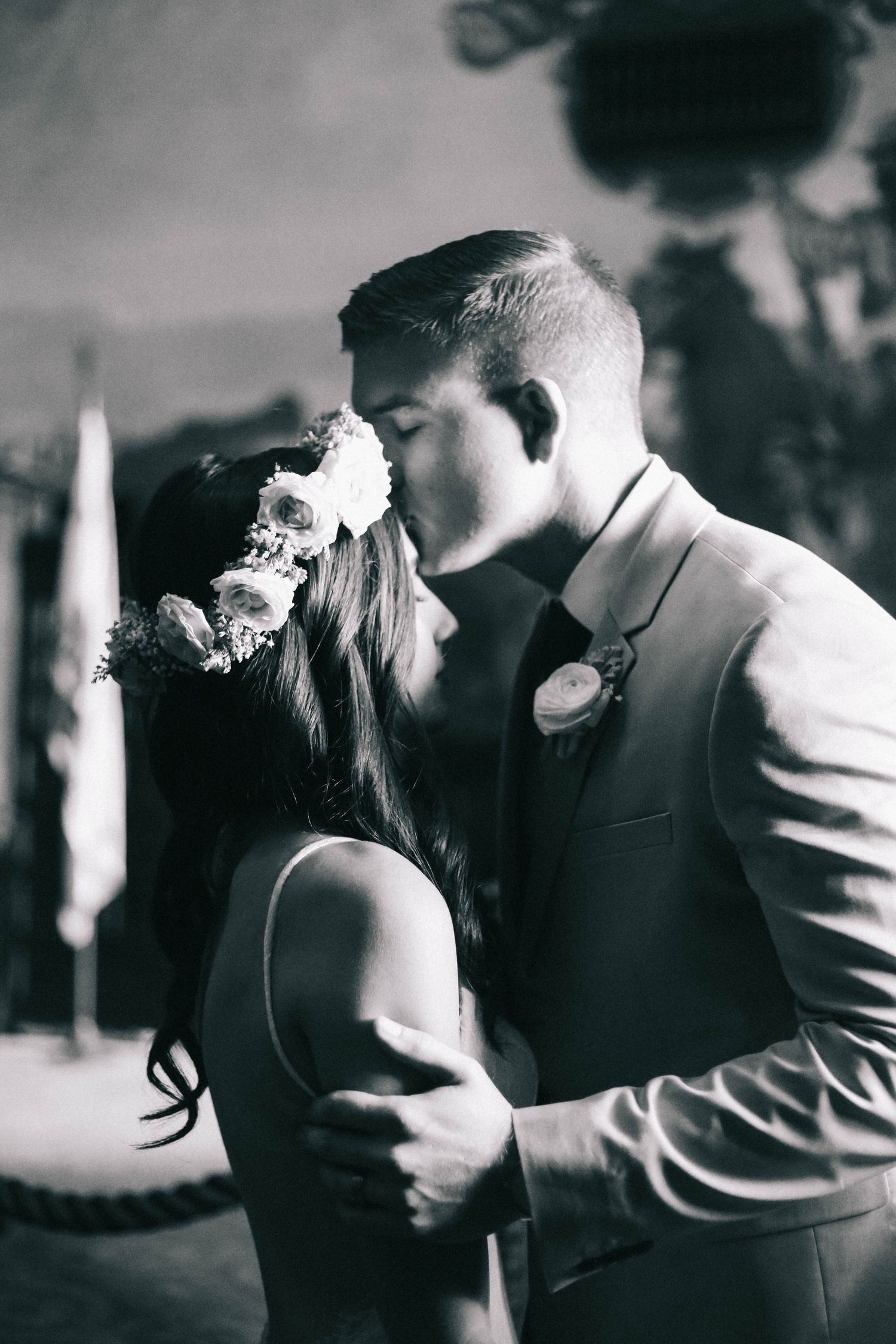 Black and white romantic kiss between bride wearing flower crown and groom in suit at wedding.