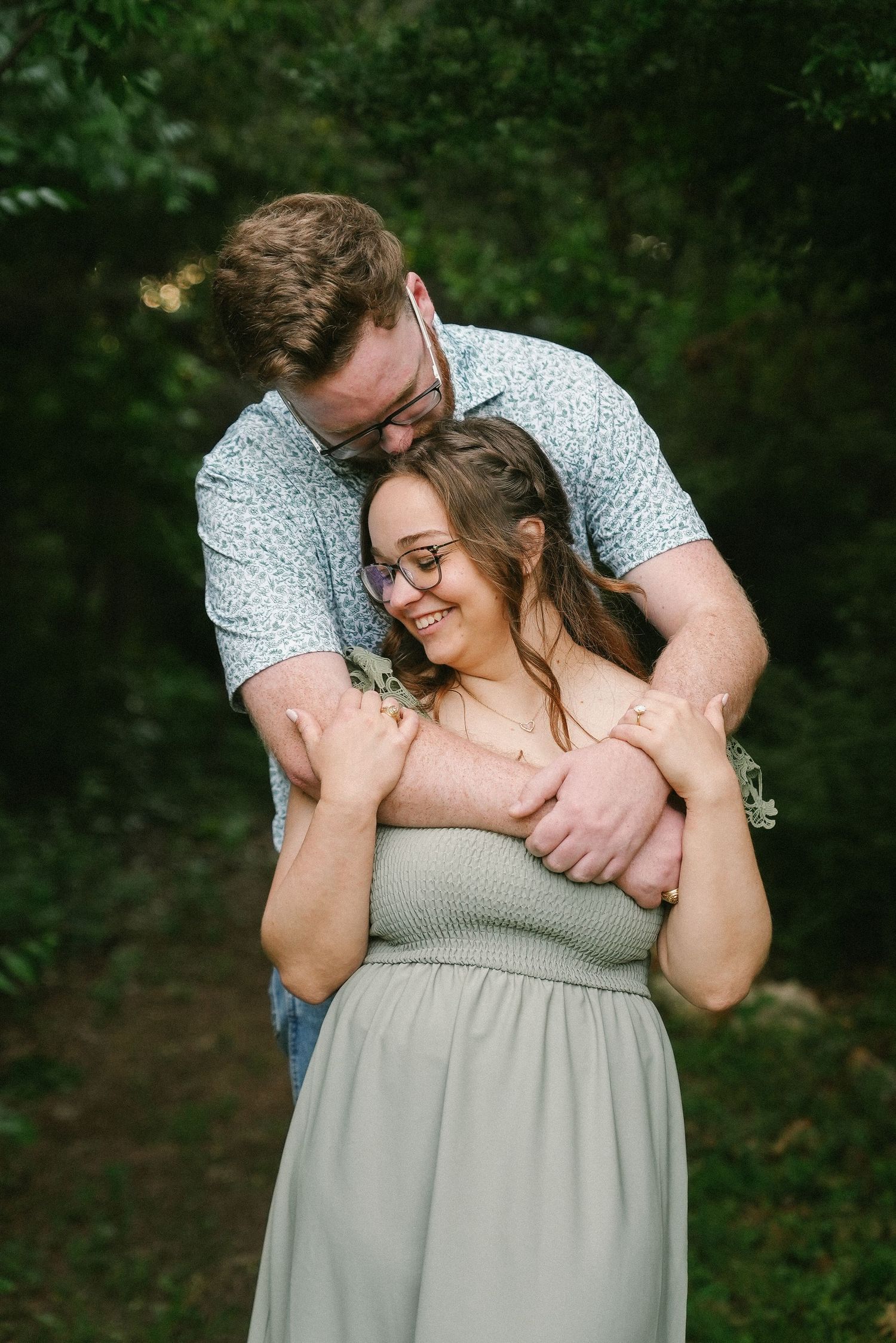 Happy couple embraces in a lush green outdoor setting during a romantic engagement photo session.