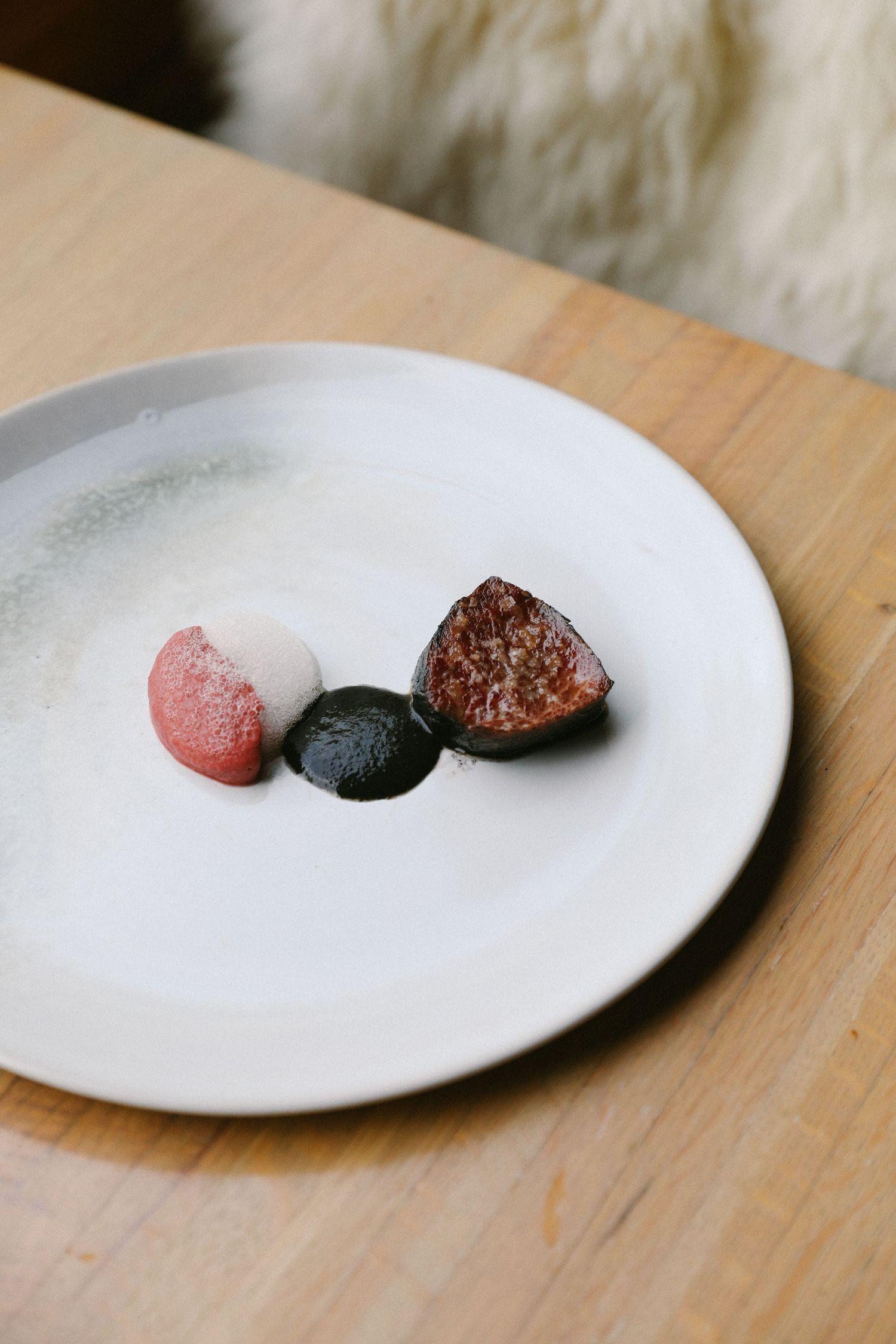 Fine dining dessert plate with pink sorbet, black chocolate disc, and fig on white plate.