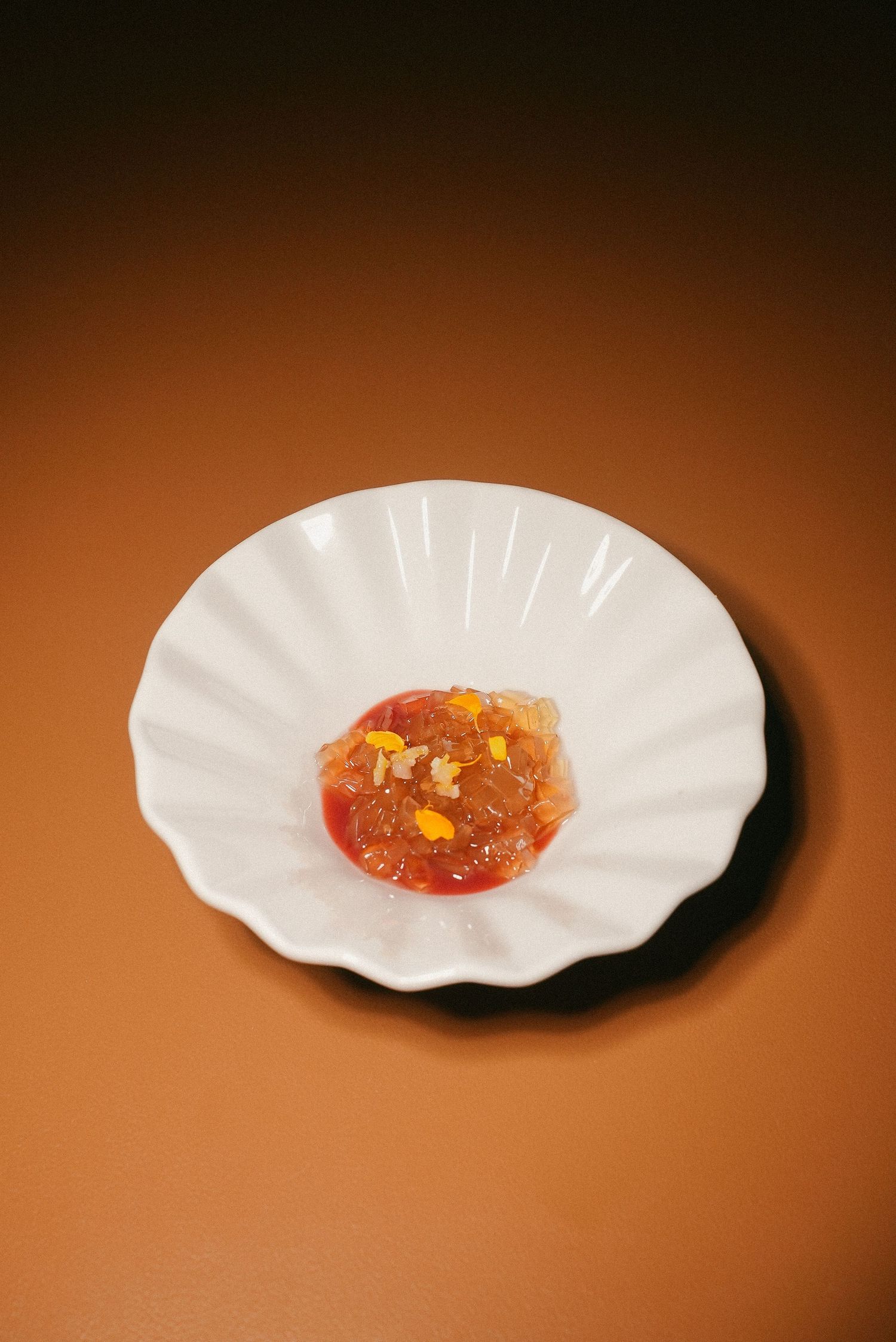 Fine dining tomato tartare with corn garnish served on a white scalloped plate.