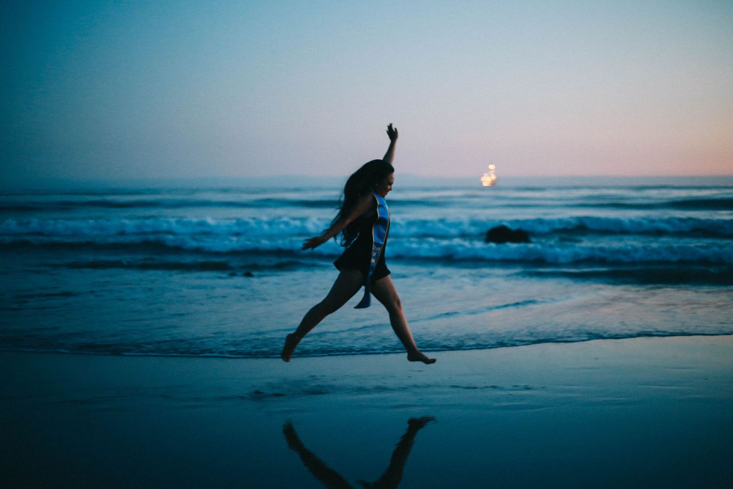 Silhouette of woman leaping joyfully on beach at sunset with ocean waves in background.