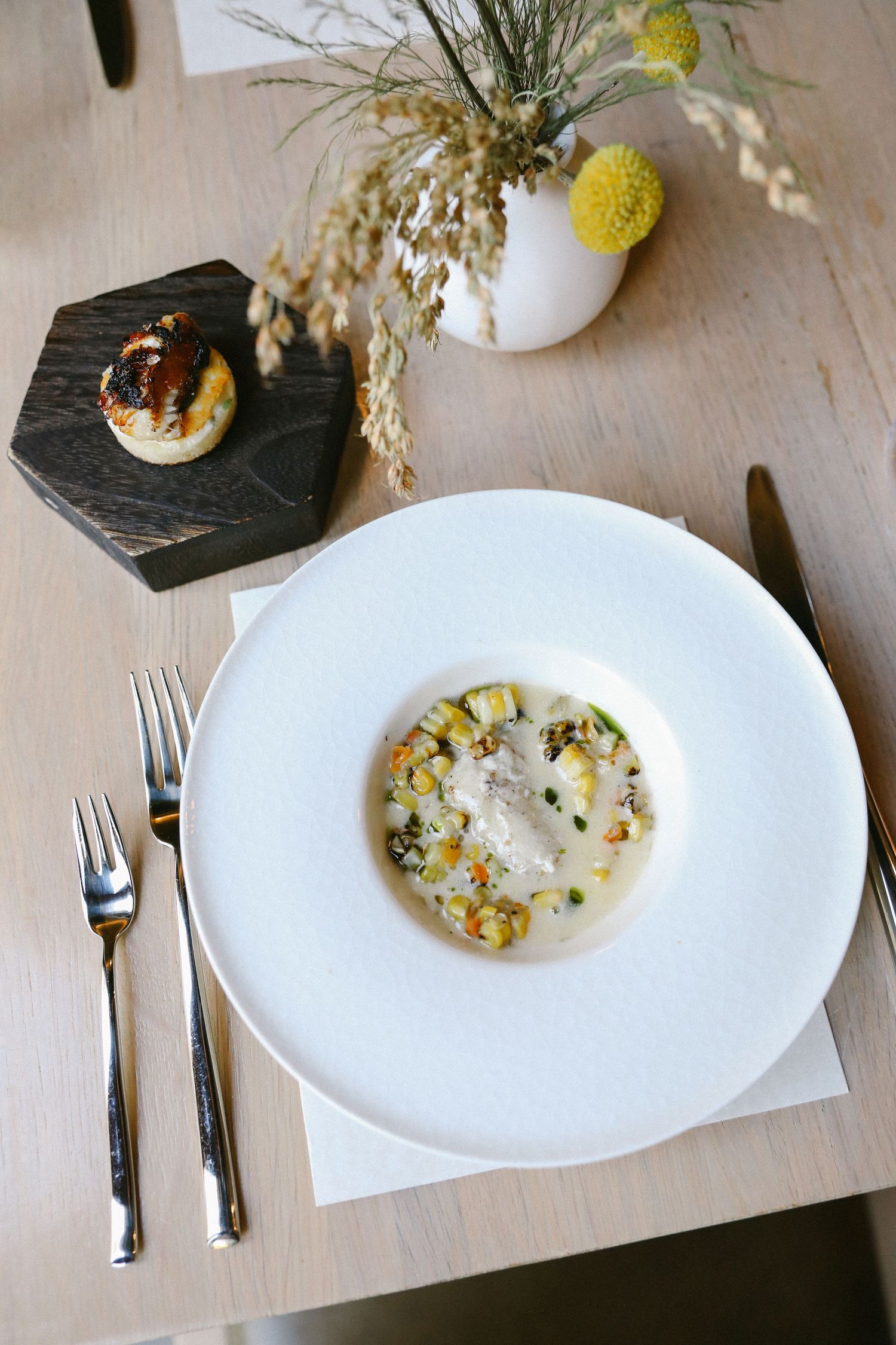 Elegant fine dining dish with corn succotash and cream sauce on white plate with silver cutlery.