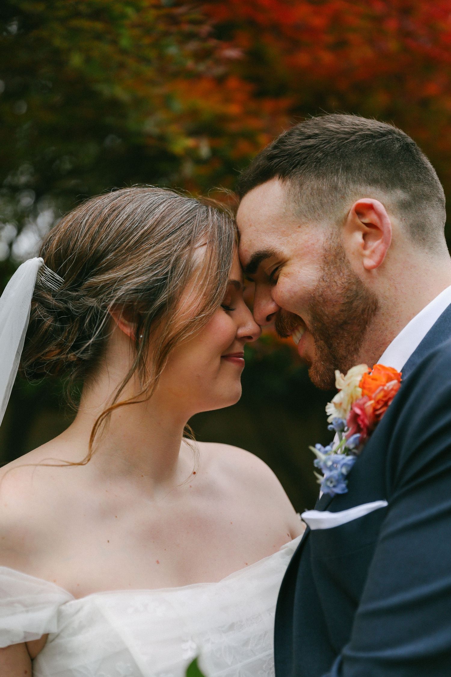 Bride and groom touch foreheads intimately with colorful autumn foliage in the background.