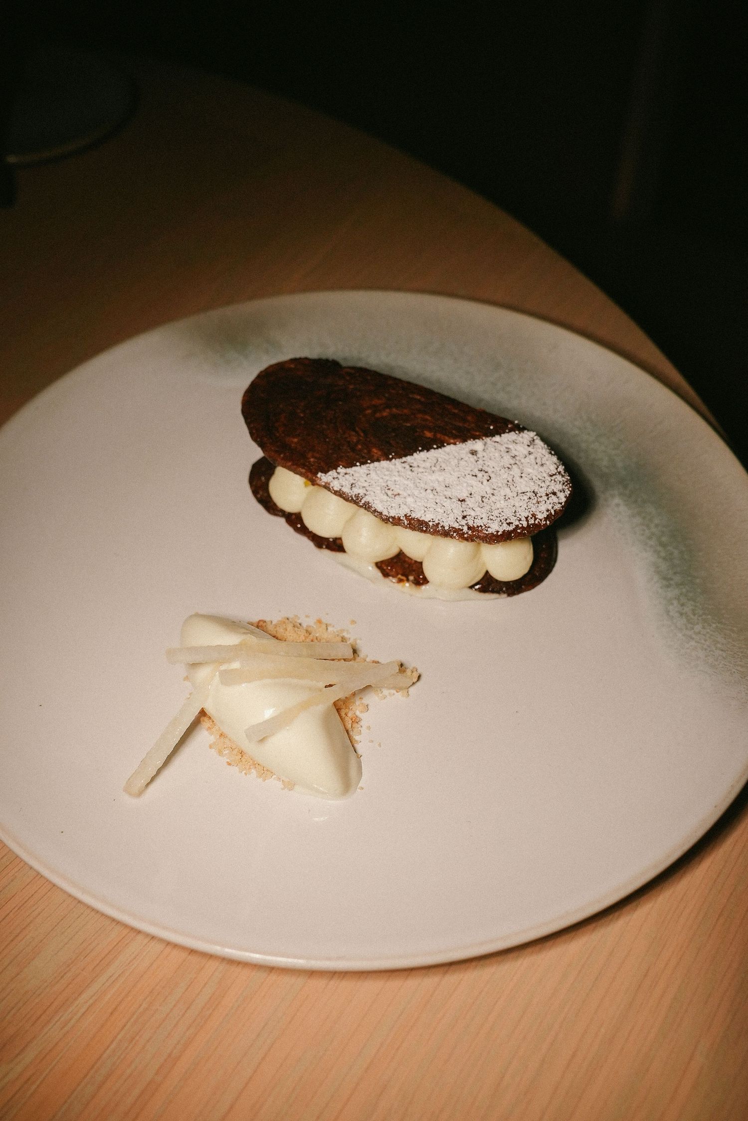 Elegant chocolate eclair dusted with powdered sugar served with white chocolate shards on a plate.