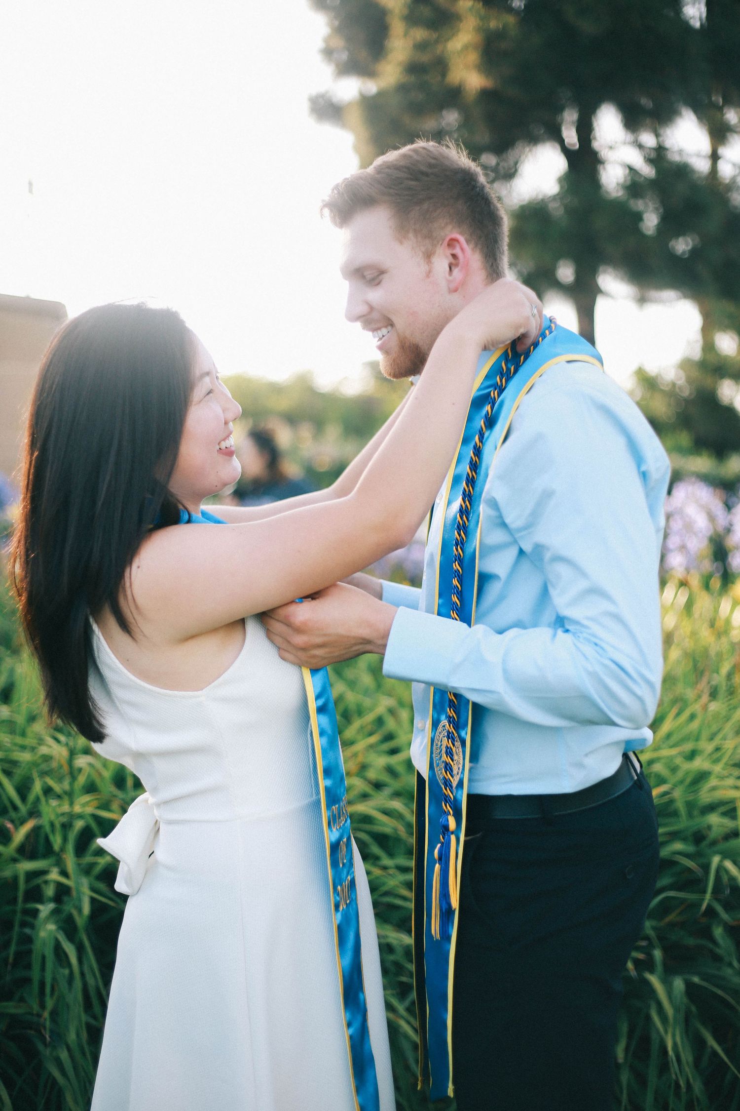 Couple sharing a tender moment outdoors with blue and gold graduation sash.
