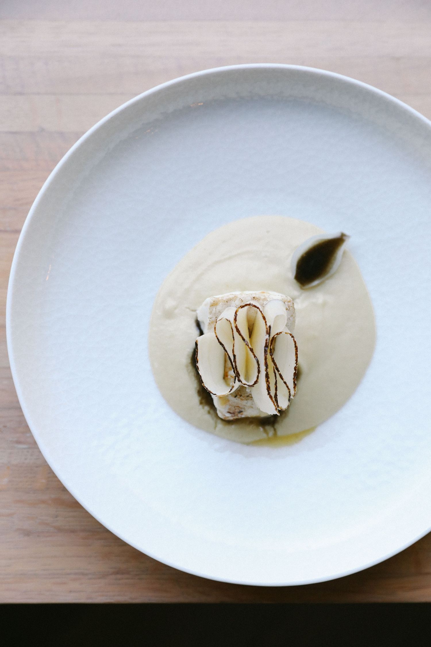 Fine dining fish fillet in creamy white sauce with almond slices and bay leaf on a white plate.
