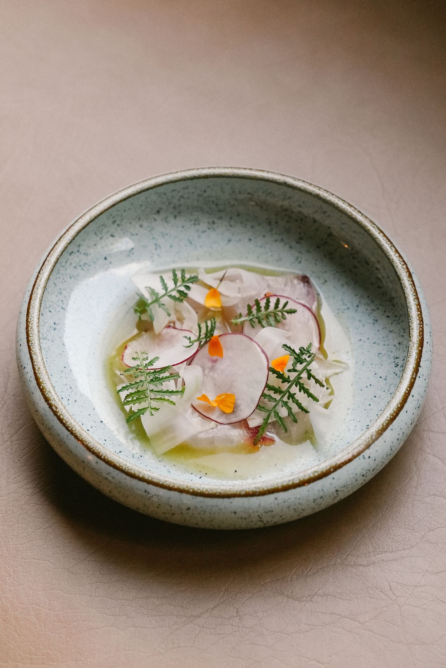 Elegant fish crudo dish garnished with radish, herbs, and edible flowers in a ceramic bowl.