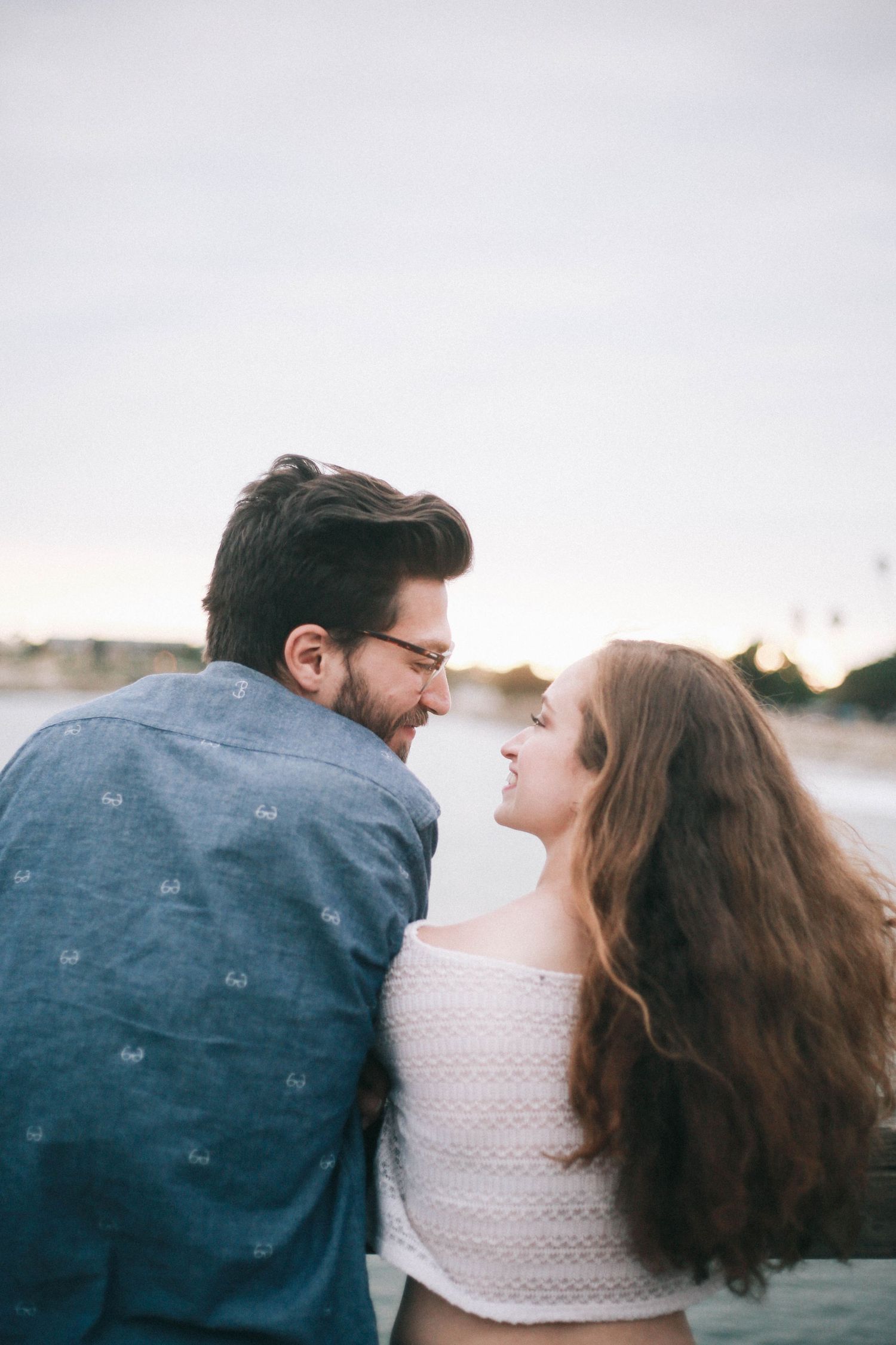 Couple smiling at each other in a tender romantic moment outdoors near the water.