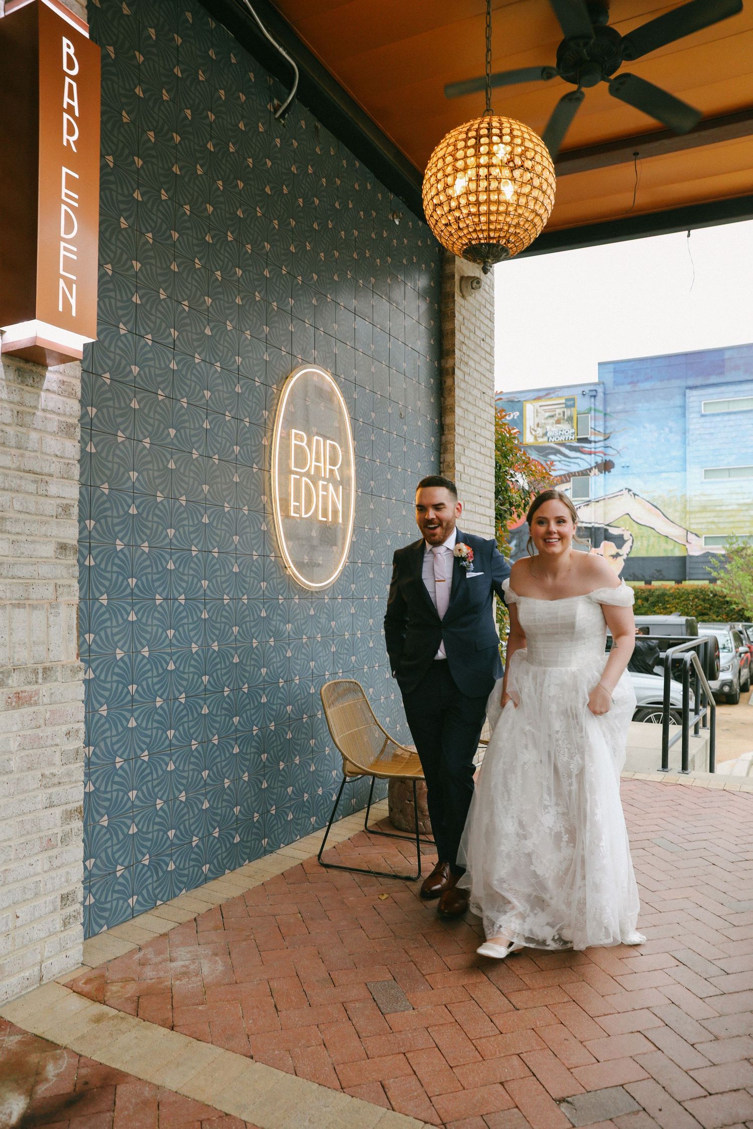 Bride and groom smiling outside Bar Eden venue entrance with decorative globe pendant light.