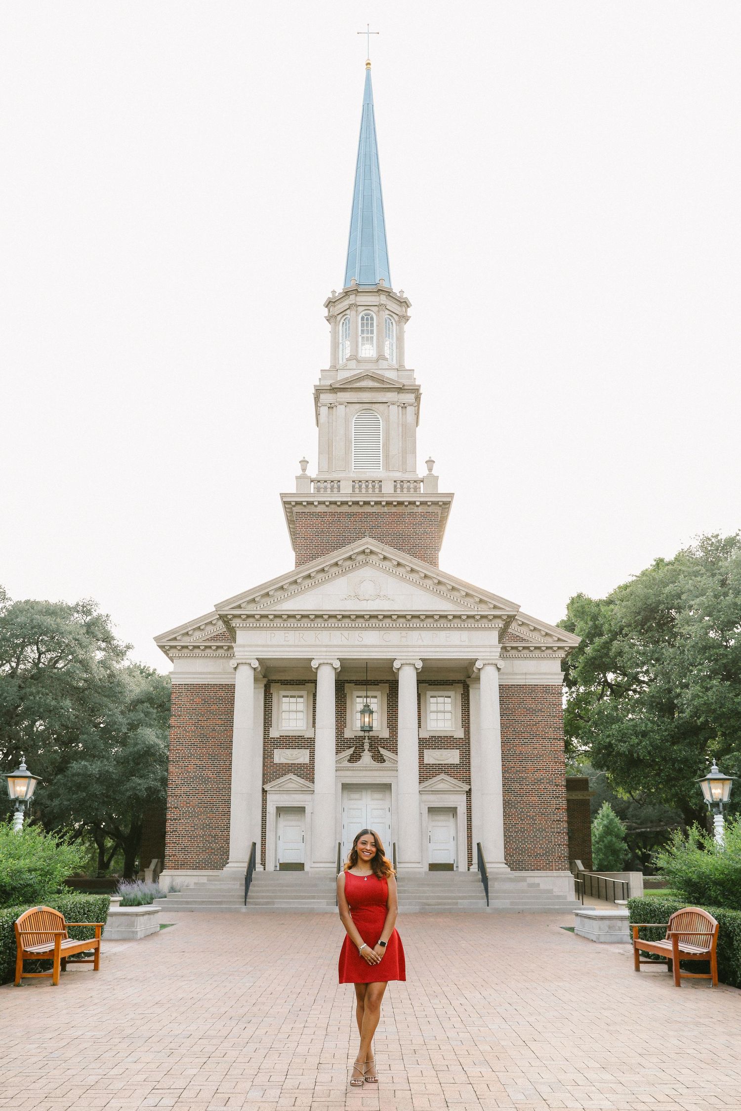 Young woman in red dress standing in front of a brick church with a blue steeple on campus.