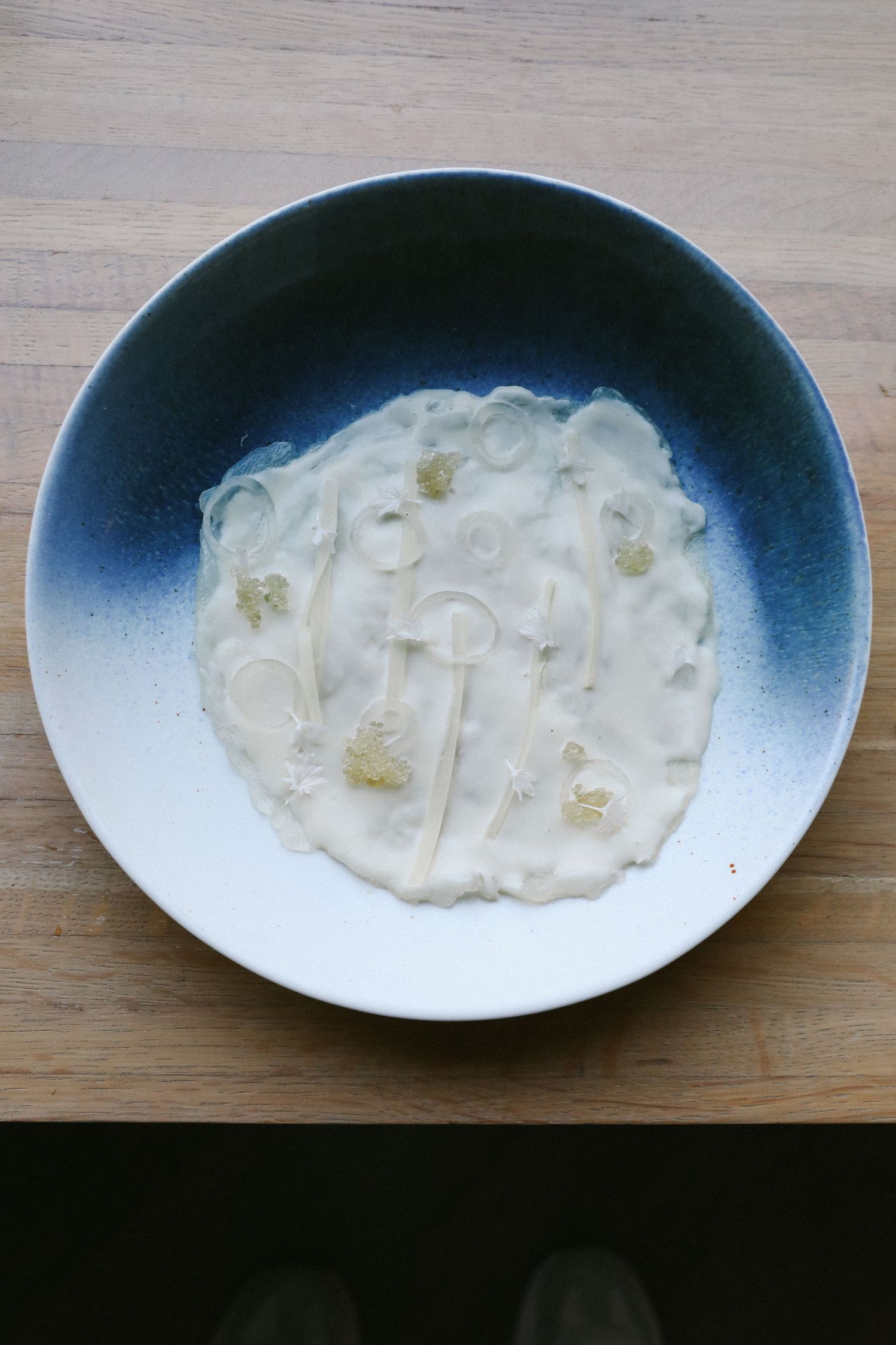 Creamy white sauce with delicate garnishes artfully presented in blue and white ceramic bowl.