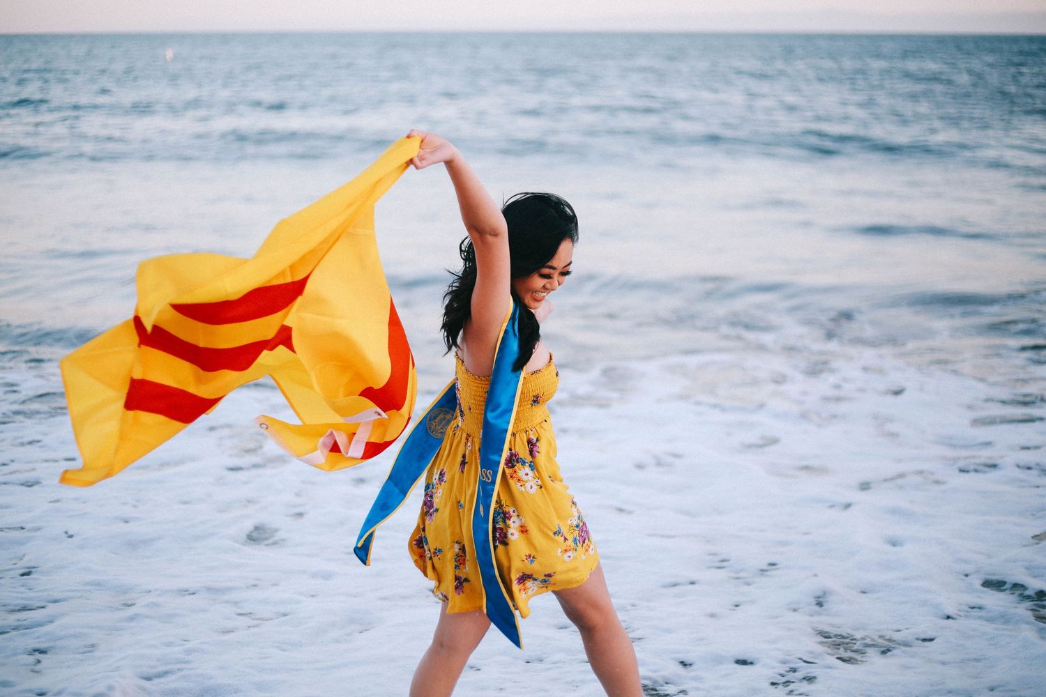 Young woman in yellow floral dress waving South Vietnamese flag at beach.