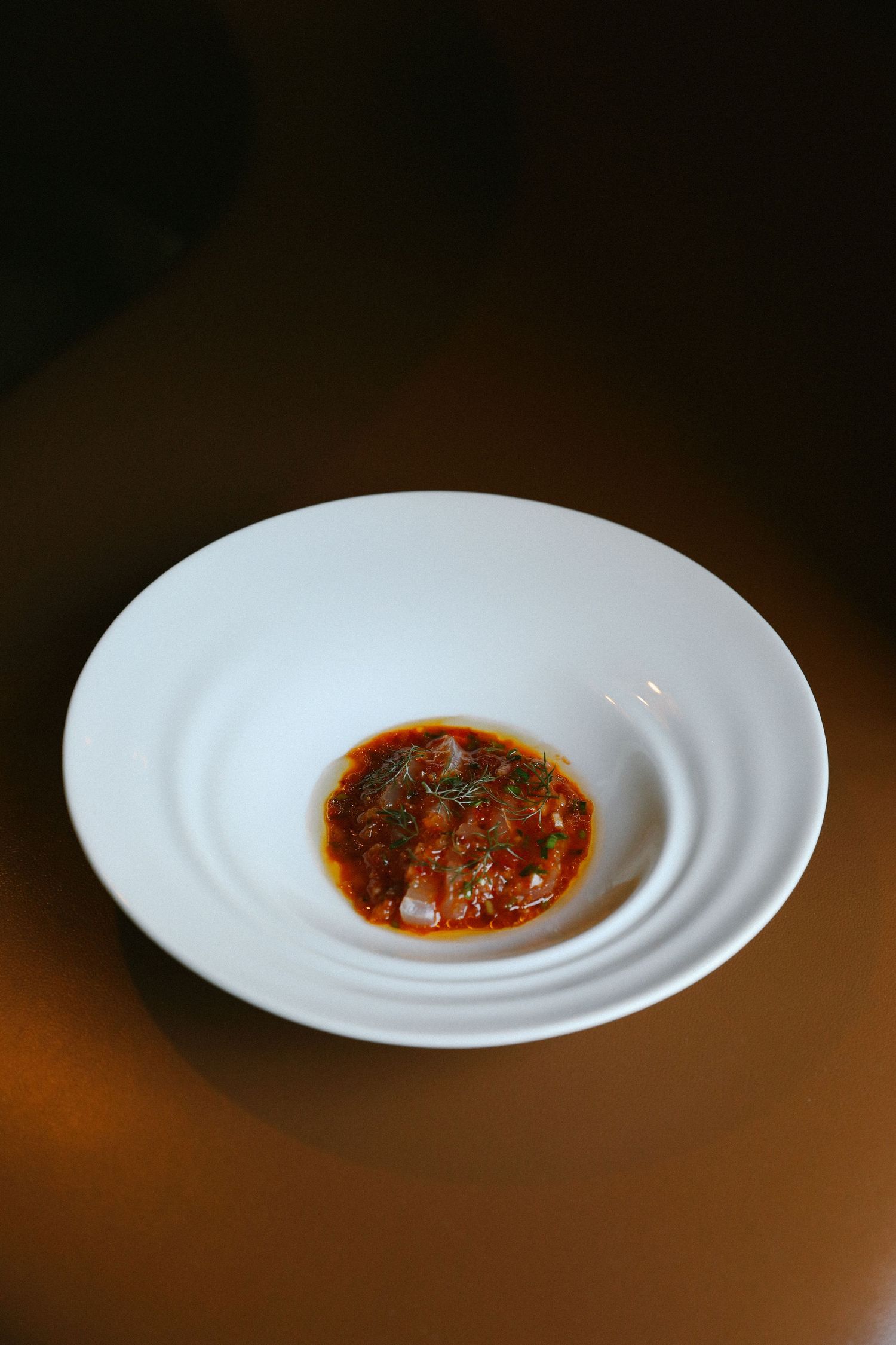 Fine dining tomato-based sauce with fresh herbs elegantly presented in white rippled bowl.