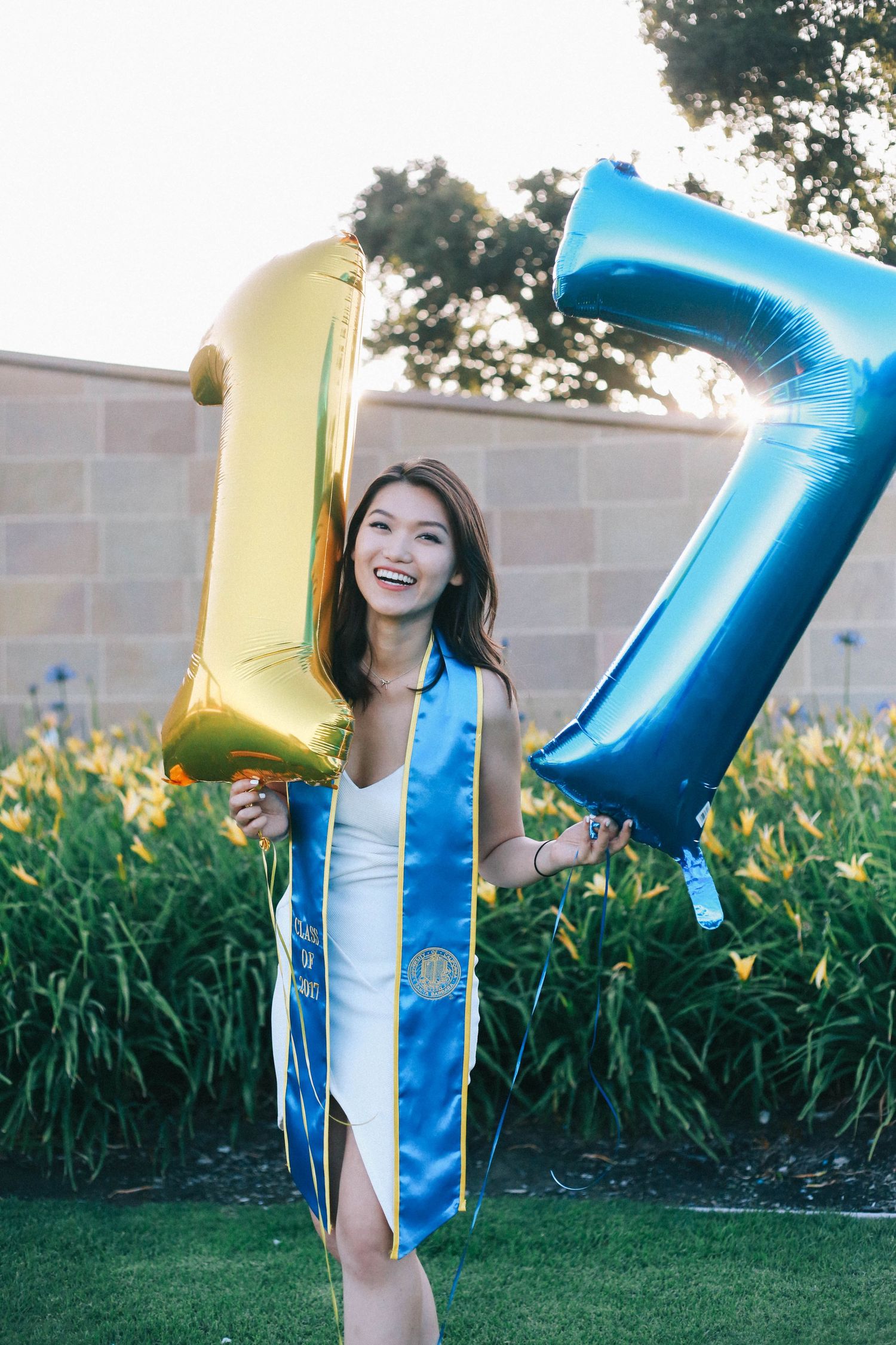 Graduating student holding gold and blue number 17 balloons wearing UCLA sash.