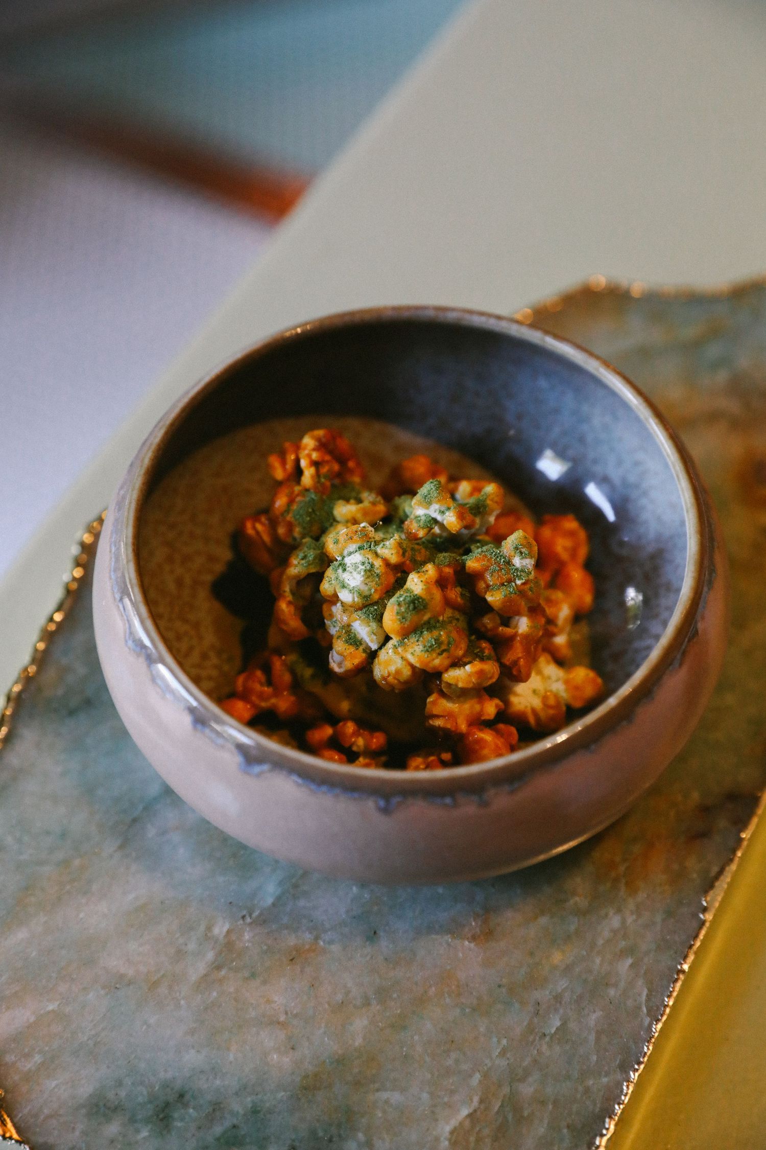 Roasted walnuts with herb seasoning served in rustic ceramic bowl on stone surface.
