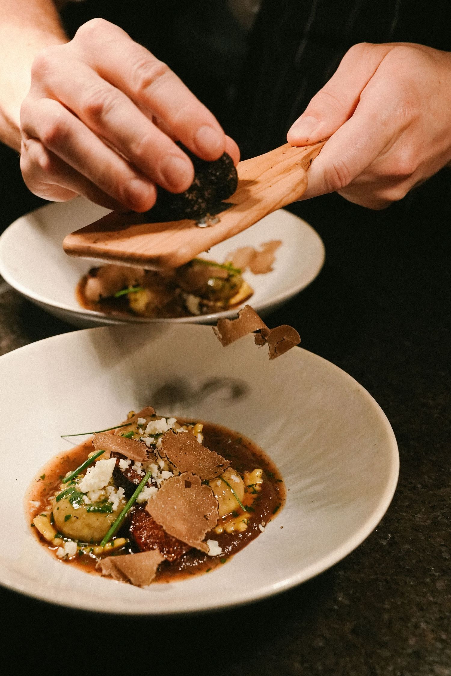 Chef garnishing gourmet dish with truffle shavings in white bowl at upscale restaurant.