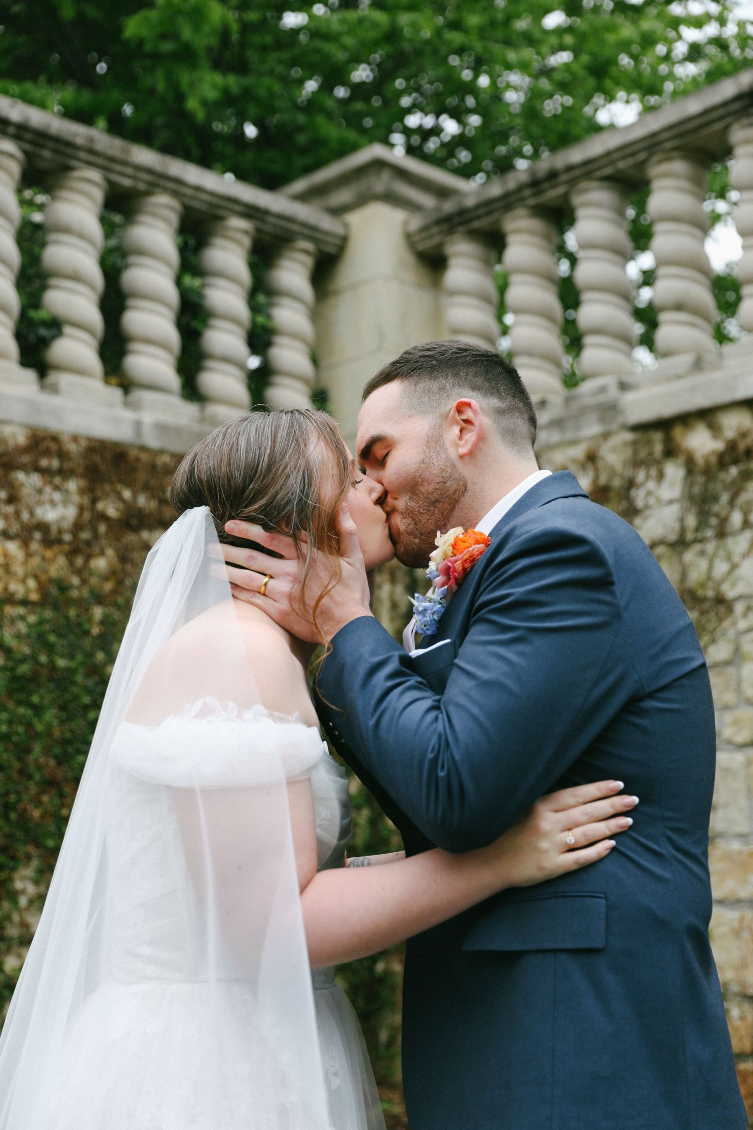 Bride and groom sharing a romantic kiss in front of stone balustrade outdoors.