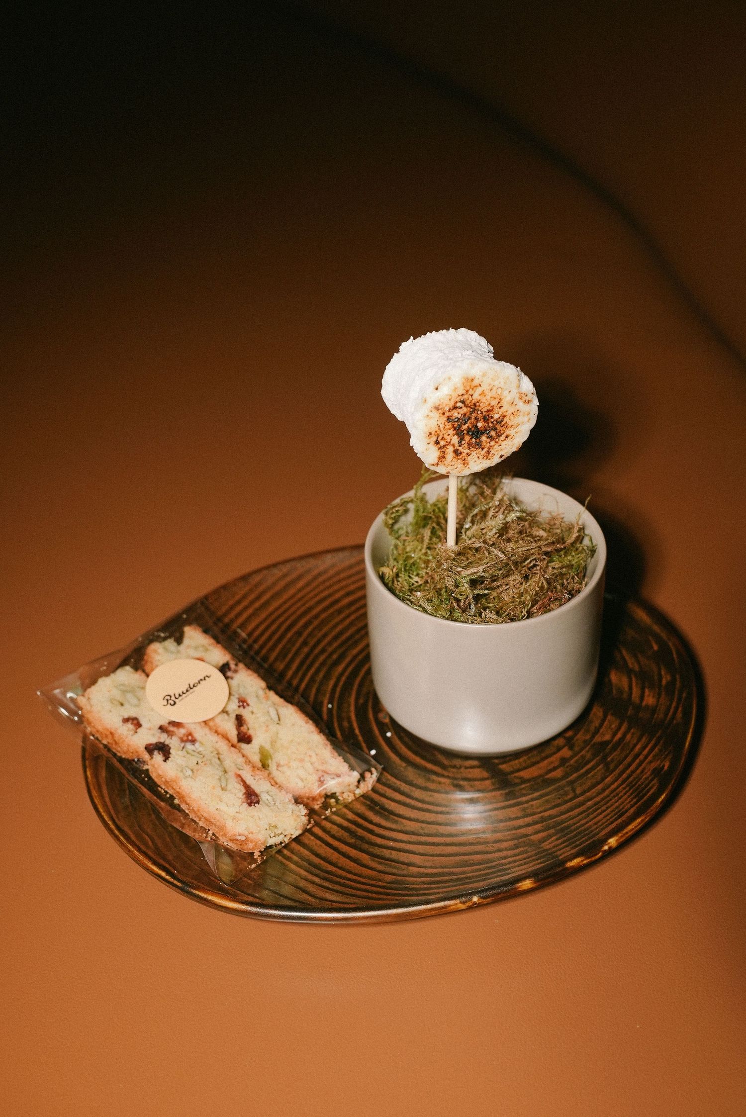 Gourmet petit fours with a toasted marshmallow lollipop in herbs and packaged nougat on glass tray.