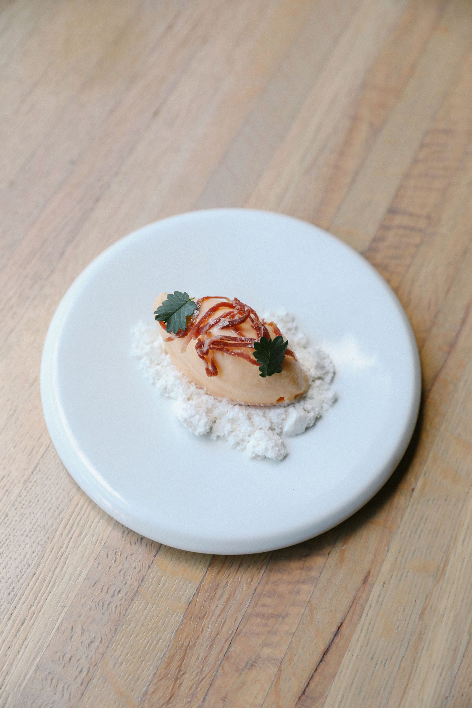 Elegant fine dining scallop with herb garnish and sauce on round white marble plate.