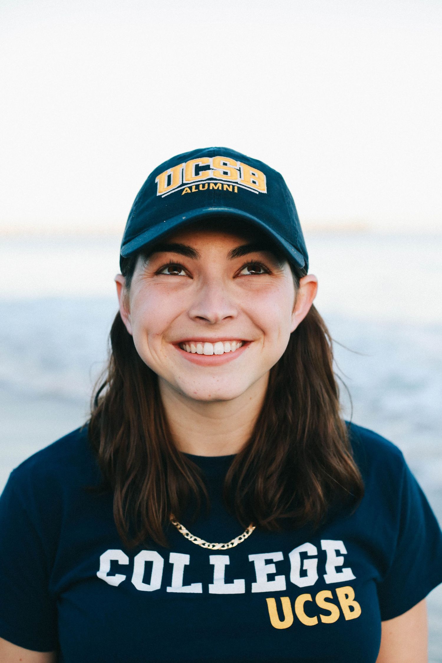 Smiling woman wearing UCSB Alumni cap and College UCSB t-shirt at the beach.