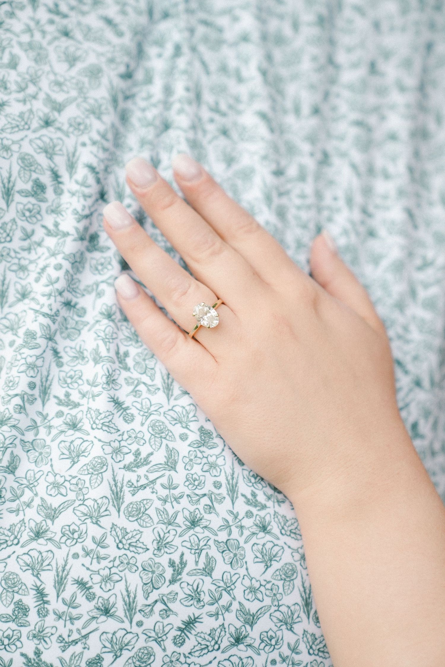 Close-up of elegant diamond engagement ring on gold band against floral patterned fabric.