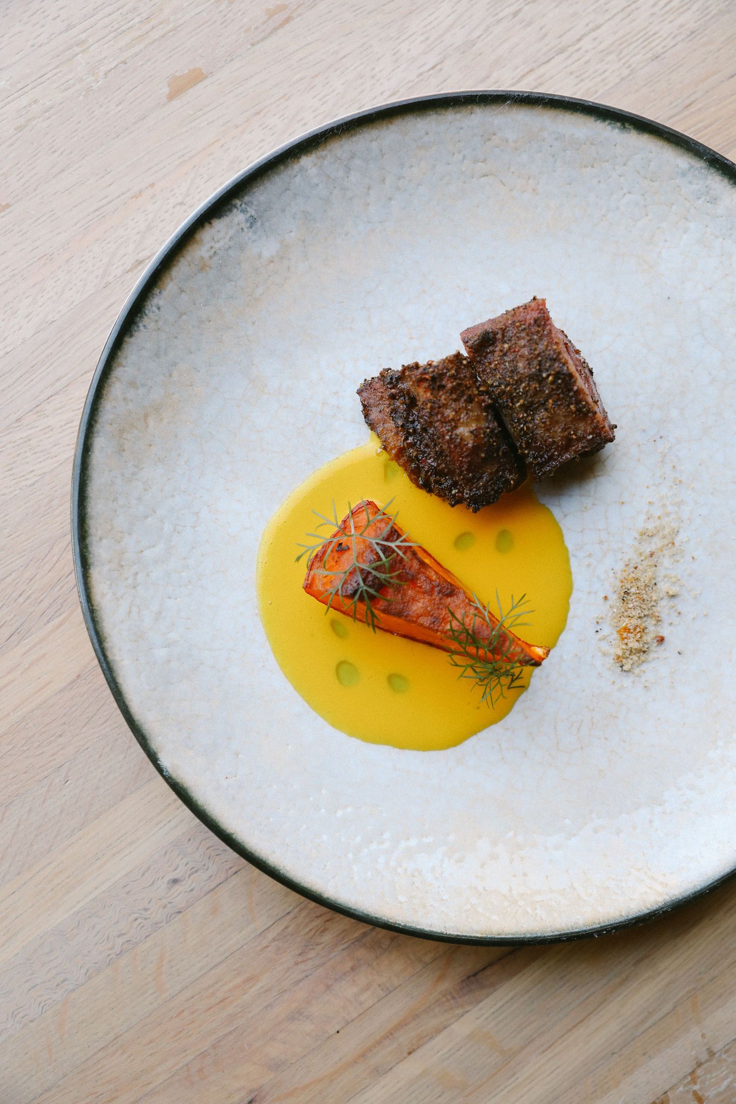 Fine dining beef with roasted carrot in golden sauce on rustic ceramic plate.