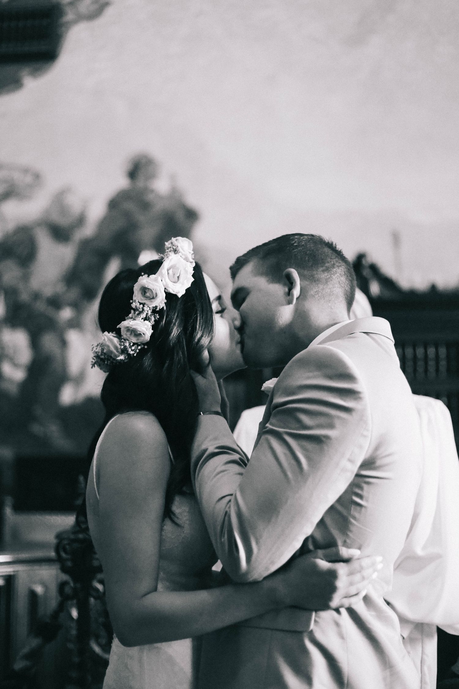 Black and white romantic wedding kiss between bride with floral crown and groom in a suit.