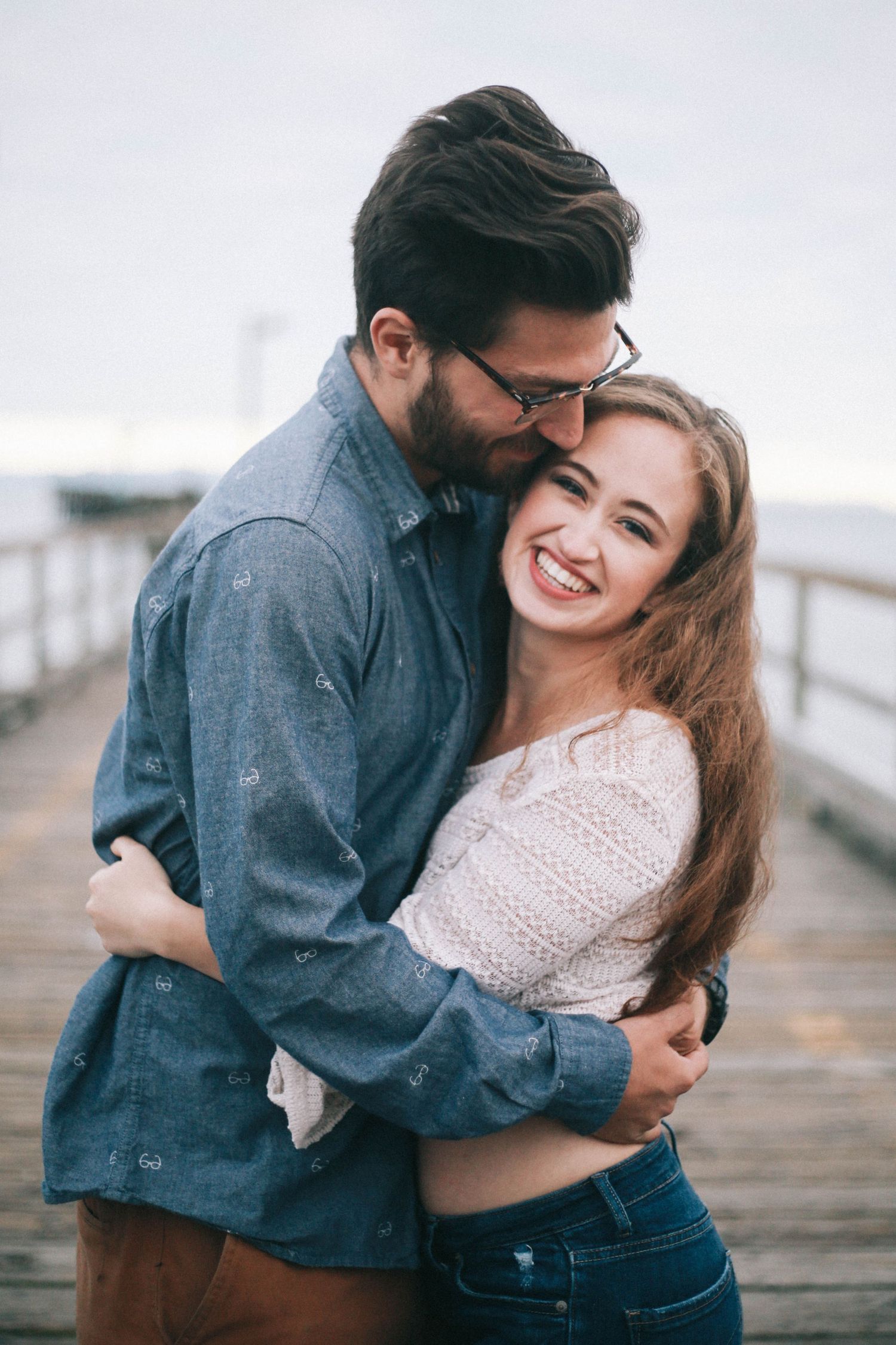 Romantic couple hugging and laughing together on a seaside wooden boardwalk.