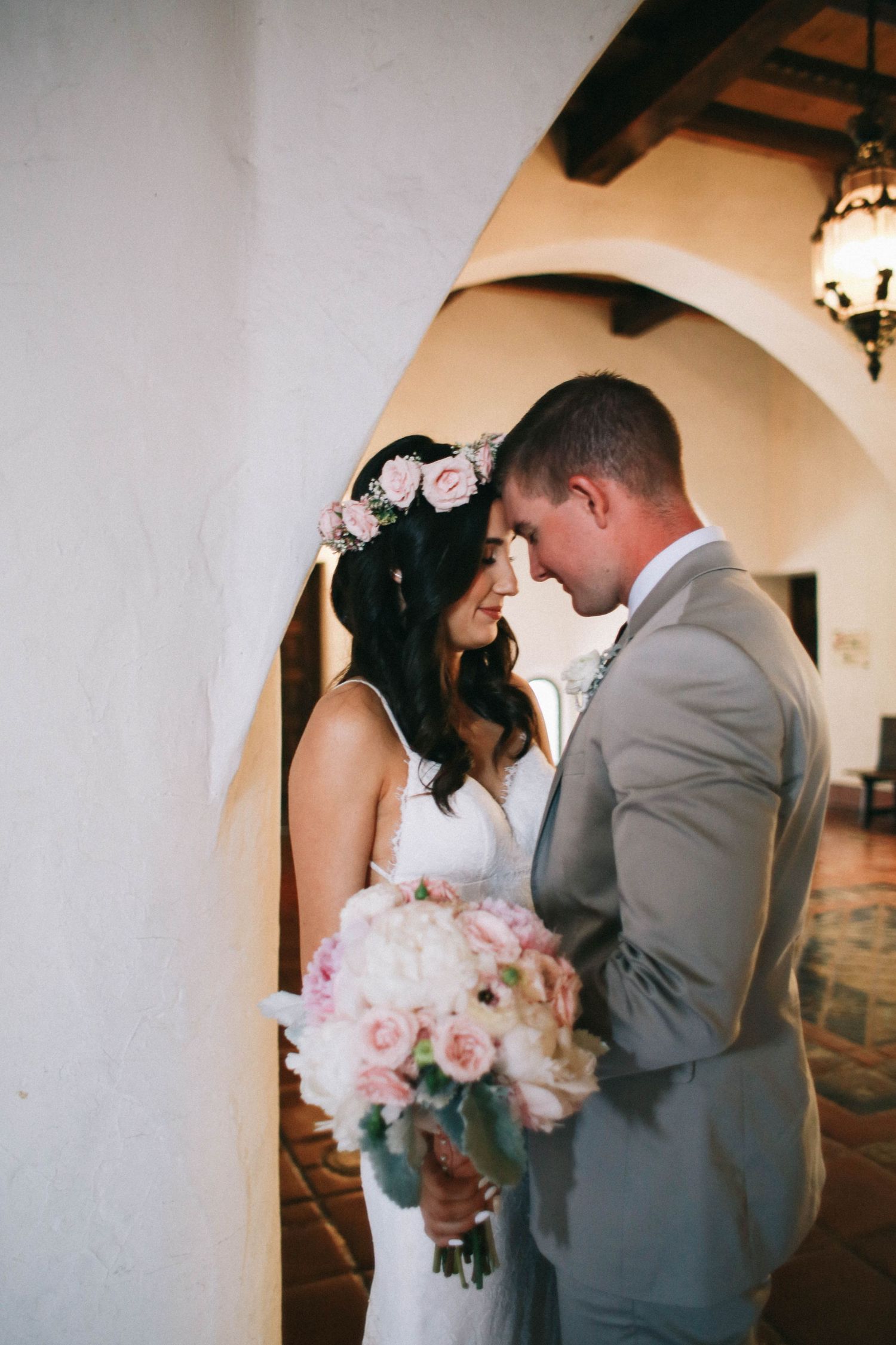 Bride and groom touching foreheads tenderly under a white arch, bride holding pink bouquet.