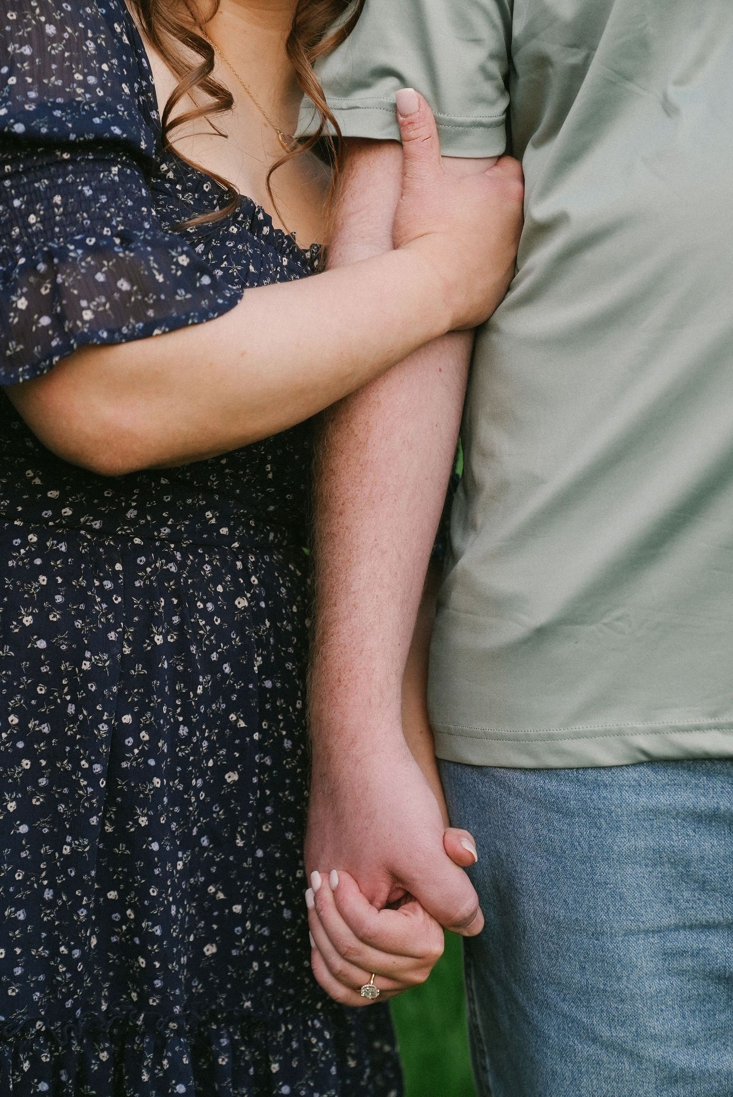 Close-up of couple holding hands, woman in navy floral dress and man in sage green shirt.
