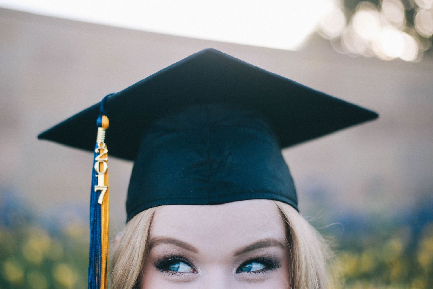Close-up of a graduate wearing a black cap with blue and gold tassel looking upward.