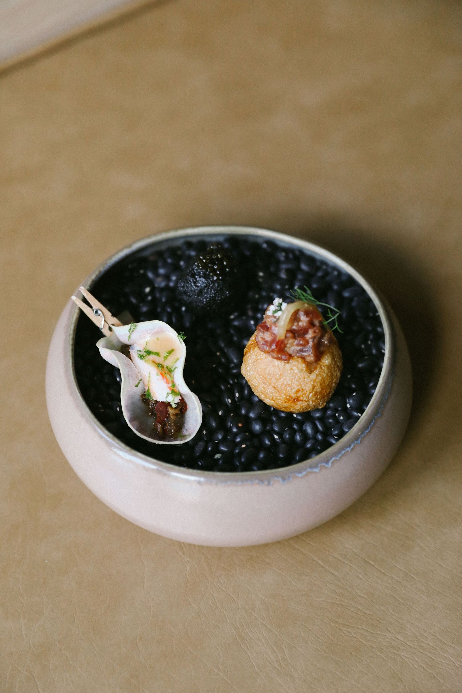 Elegant amuse-bouche presentation with two bite-sized morsels in black salt bowl.